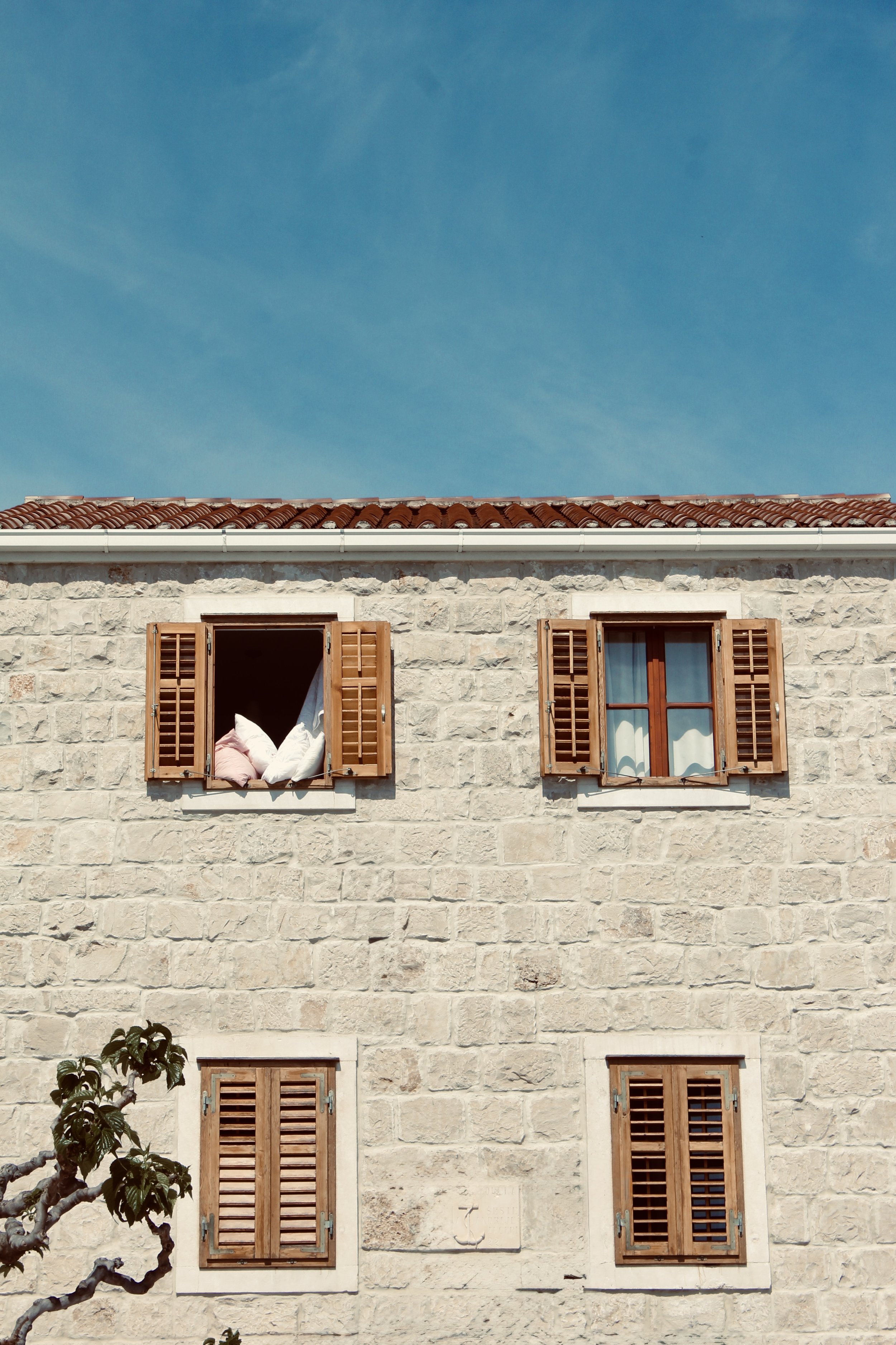 Stone building with four windows, three open with wooden shutters, one closed, against a clear blue sky.