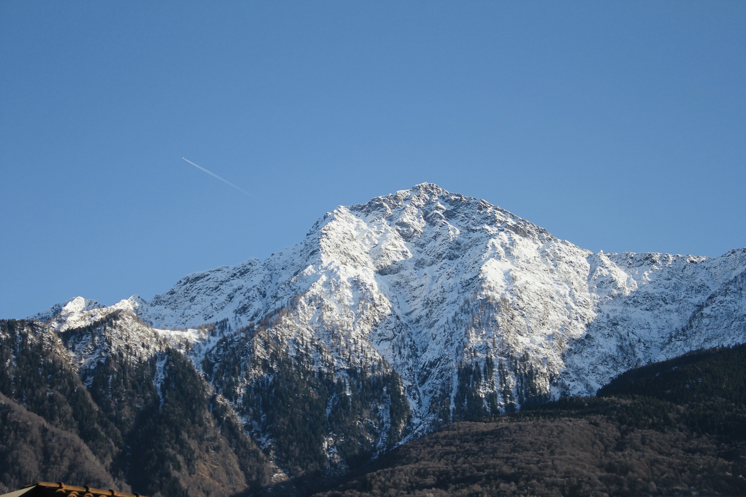 Snow-covered mountain peak with a clear blue sky and a faint airplane contrail.