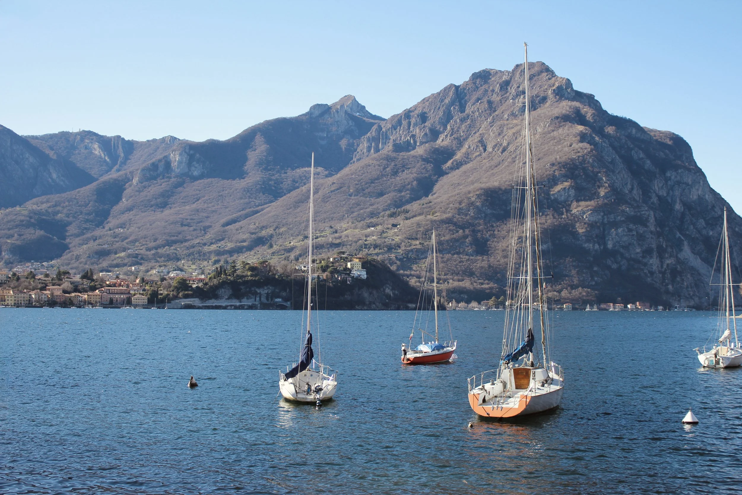 Boats anchored on a lake with a mountainous landscape and clear blue sky in the background.