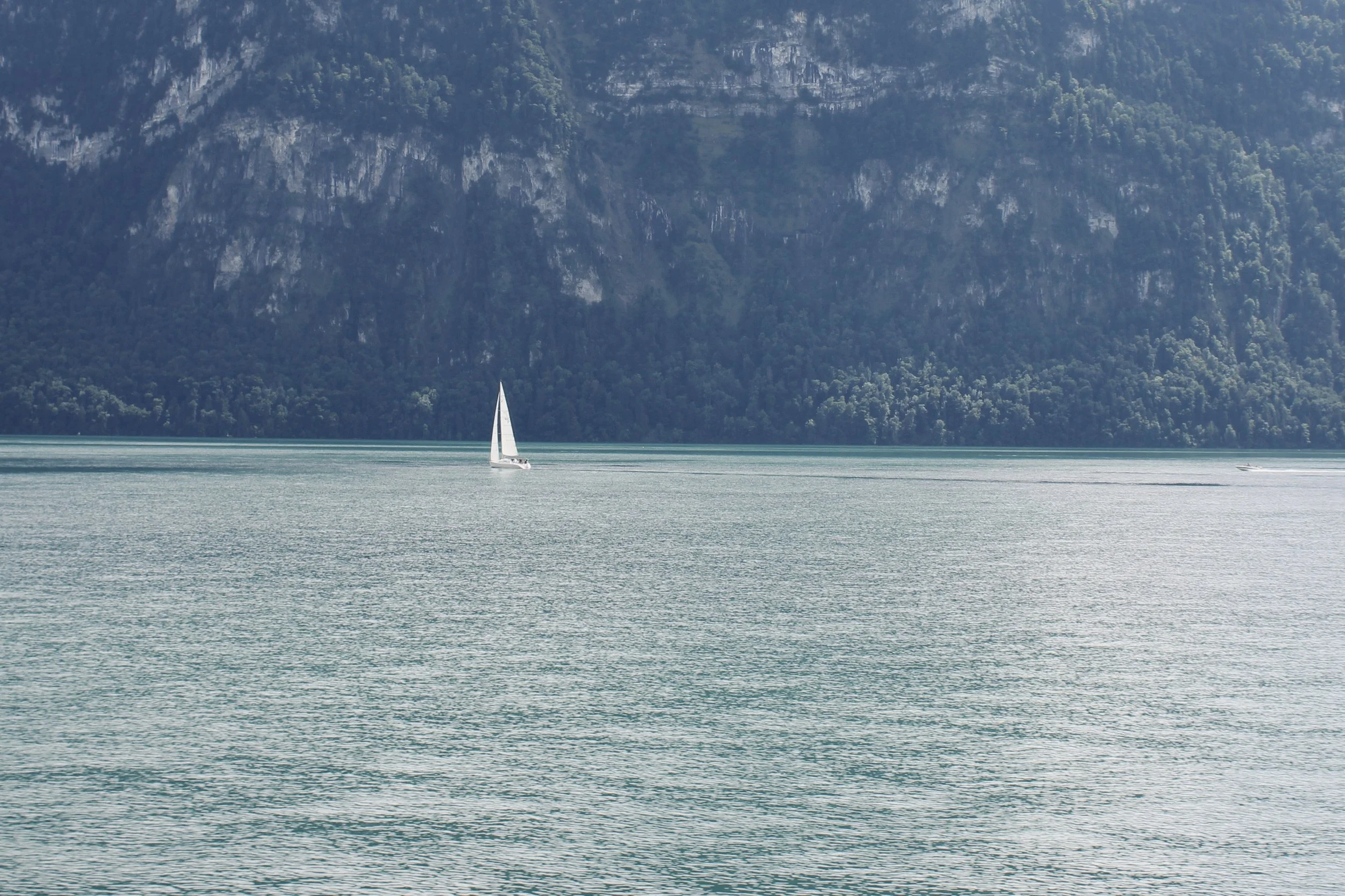 A sailboat is sailing on a calm lake with mountainous terrain in the background.