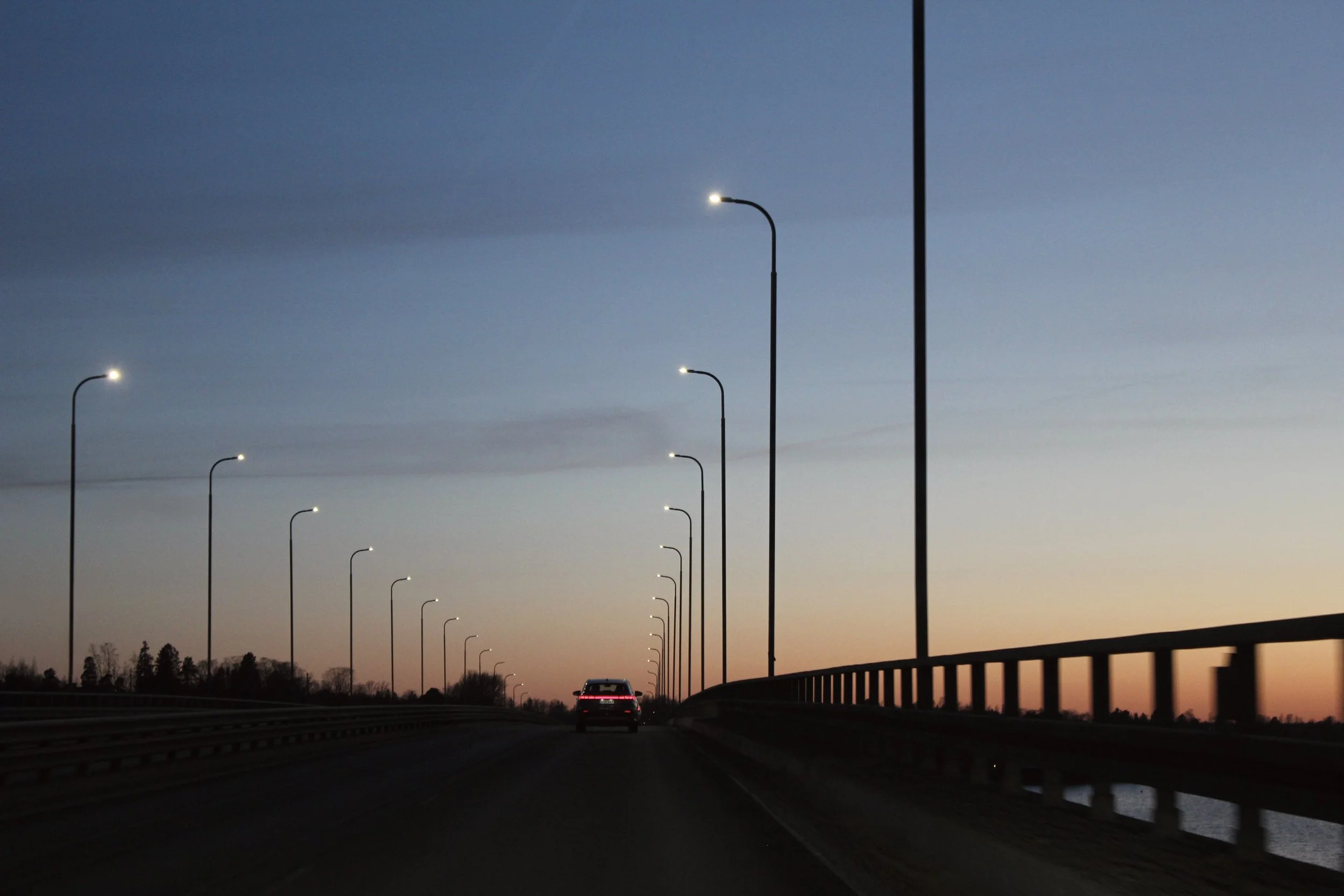 A car driving on a highway at dusk or dawn with streetlights and a scenic sky.