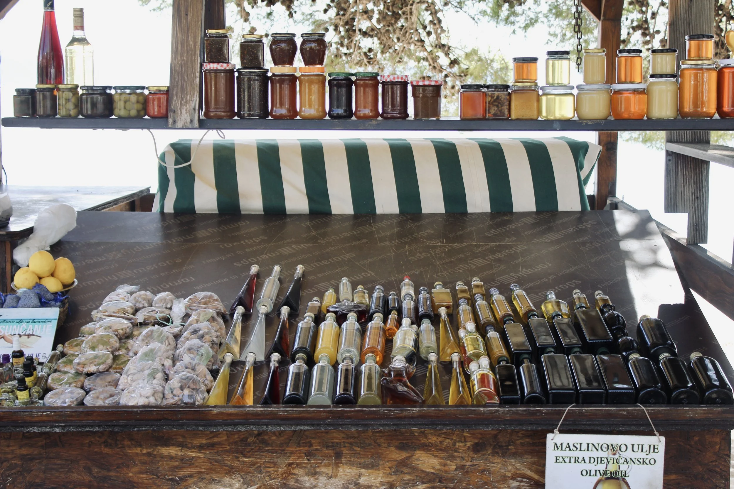 Display of various jars of oils and preserved foods on a wooden stand at an outdoor market.