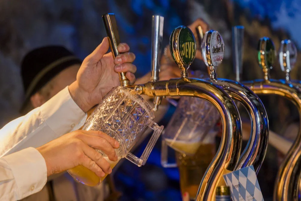 Person fyller ett glas med öl från en ölkran på en bar, flera ölkranar syns i bakgrunden.