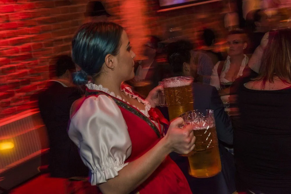 En flicka i traditionell klädsel som håller två stora ölglas i en bar