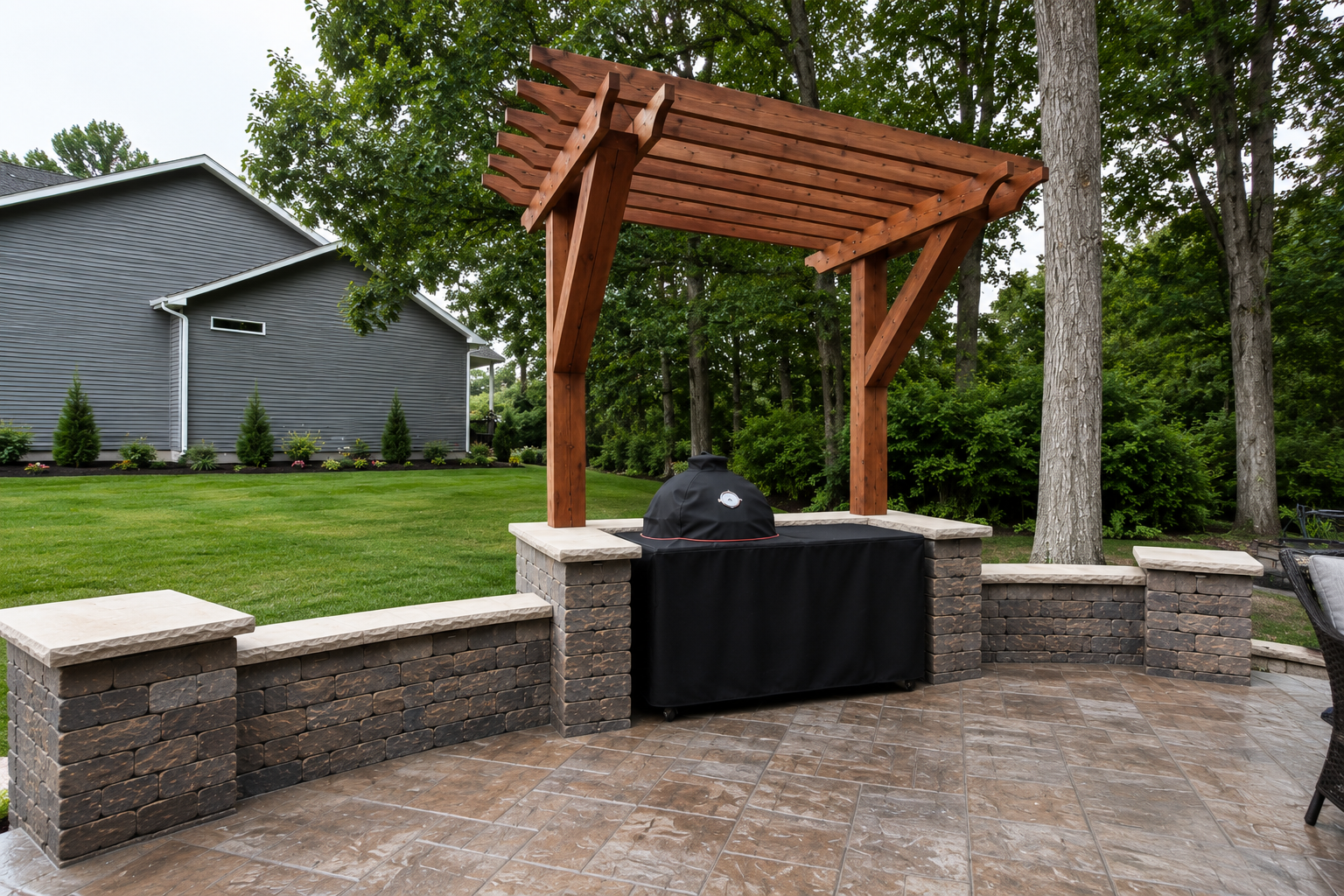 Outdoor patio area with a brick built barbecue under a wooden pergola, surrounded by green lawn, trees, and a house in the background.