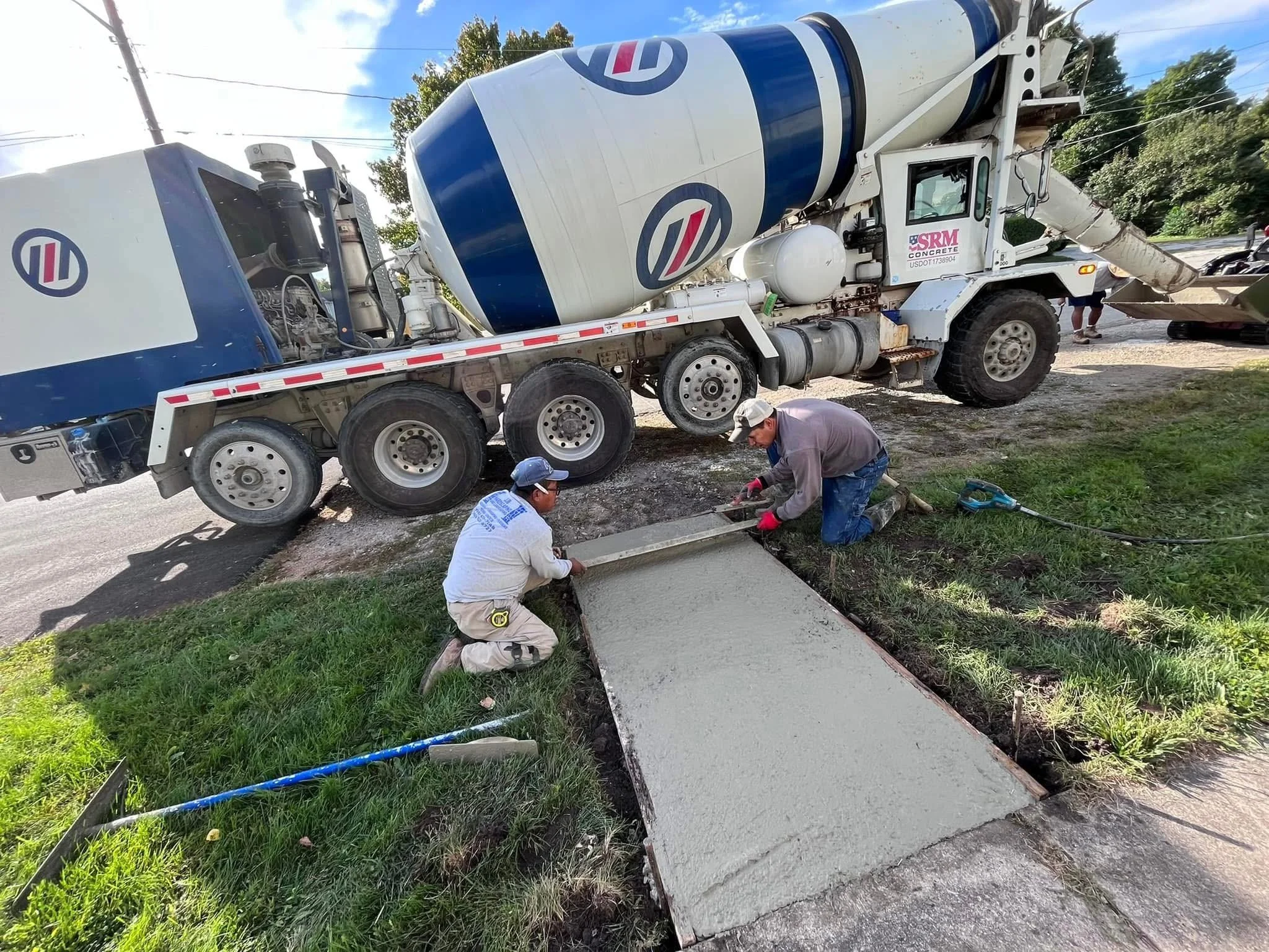Workers pouring concrete onto a sidewalk from a large cement mixer truck.