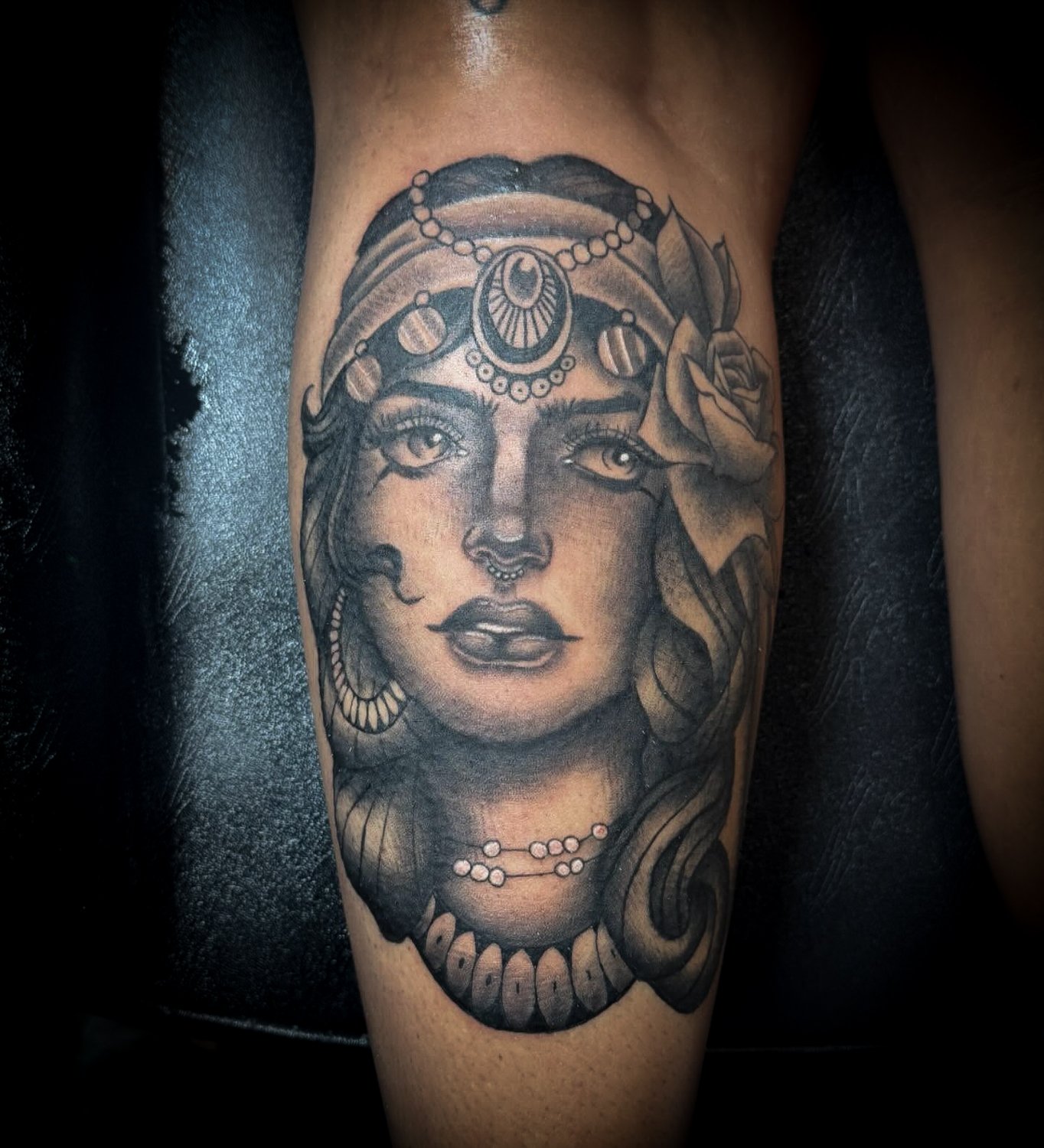 Tattoo of a woman's face with jewellery, roses, and decorative elements on arm.