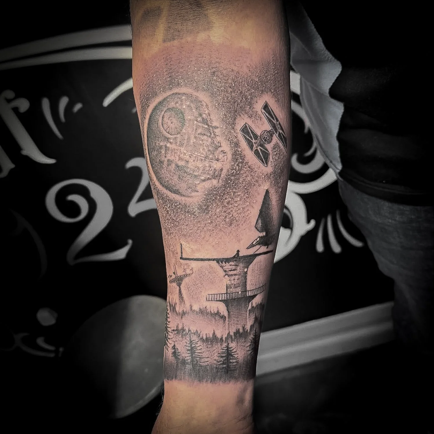 Tattoo of the Death Star from Star Wars, TIE fighter, and landscape with trees on a person's arm.