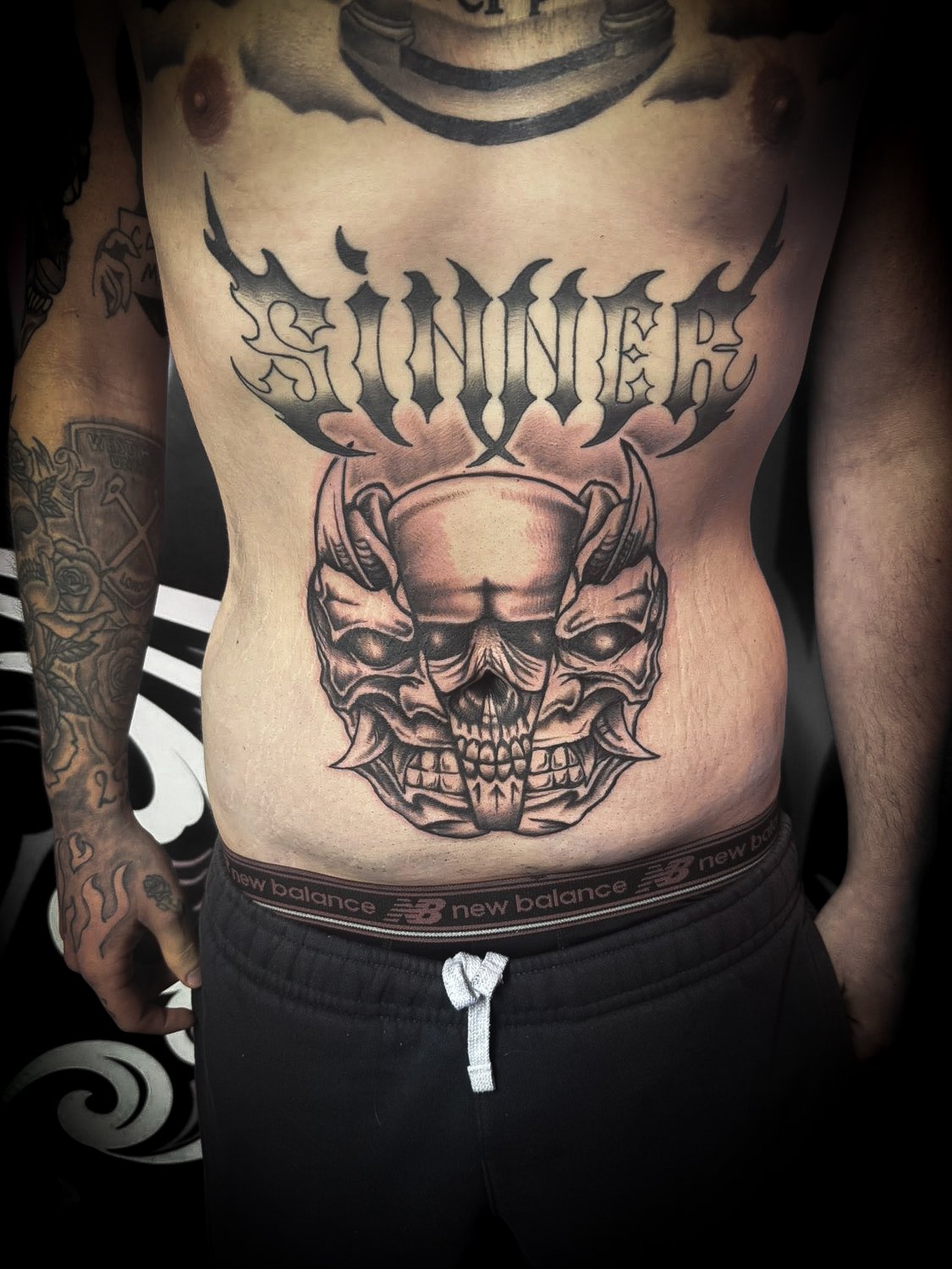 Tattoo of a skull with horns and intricate details on a person's lower chest.