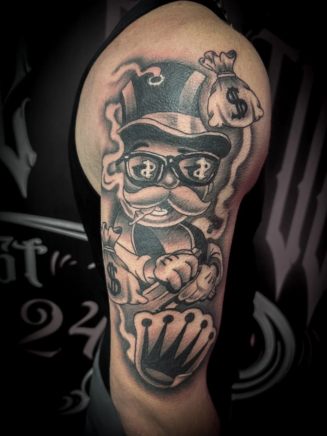 Tattoo of a cartoonish character with a mustache, wearing sunglasses with dollar signs, a top hat, smoking a cigar, holding a cane, and carrying a bag of money, on a person's upper arm.