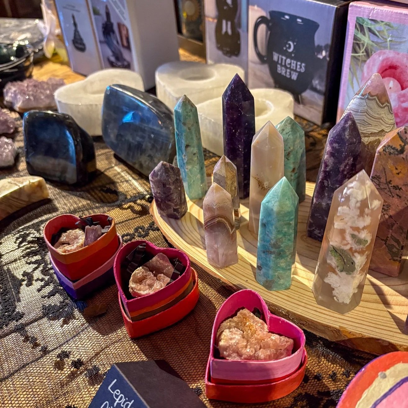 A display of various colorful crystals and gemstones on a table, with some in heart-shaped containers and others arranged on a wooden board.