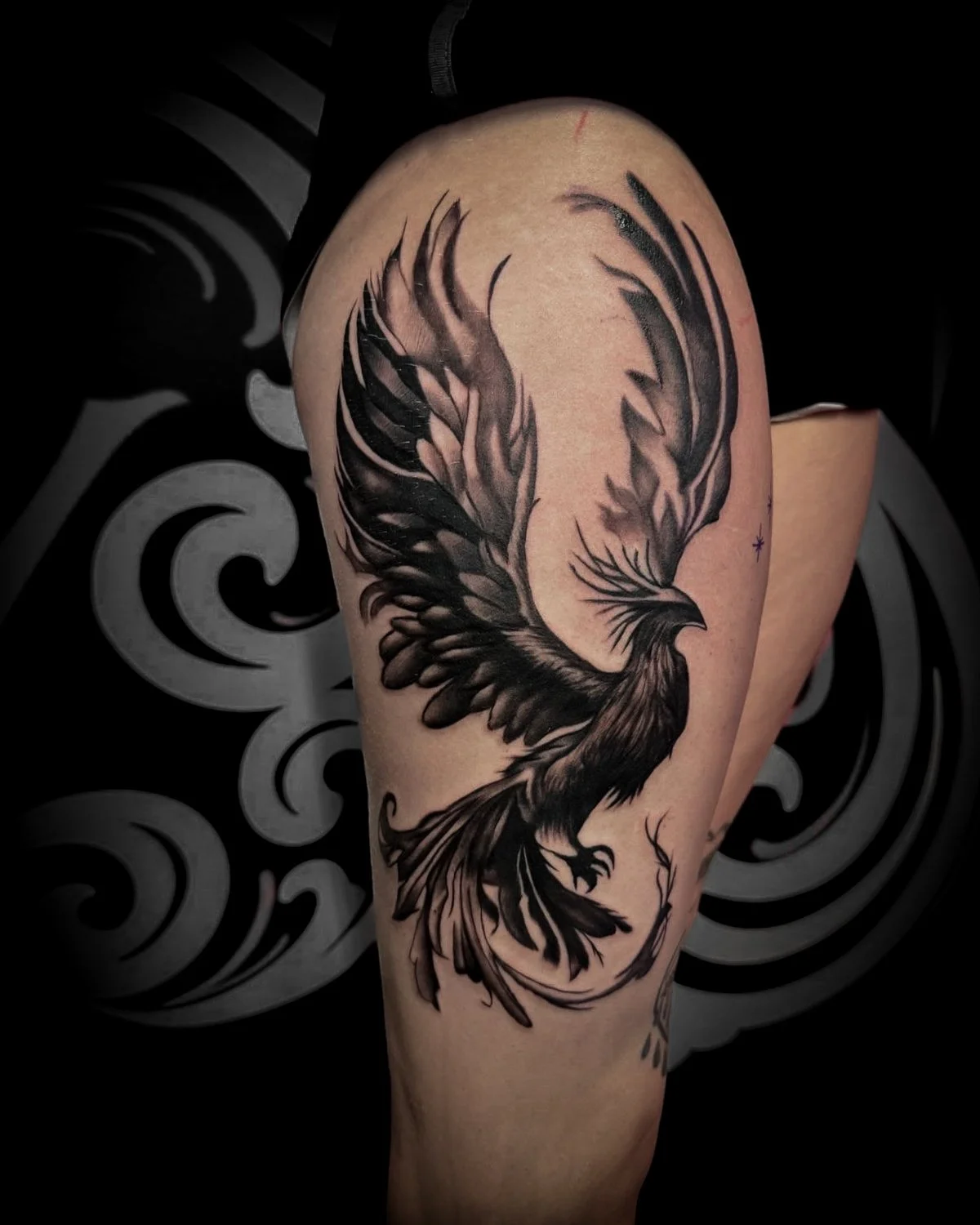 Black and gray phoenix tattoo on person's upper thigh.