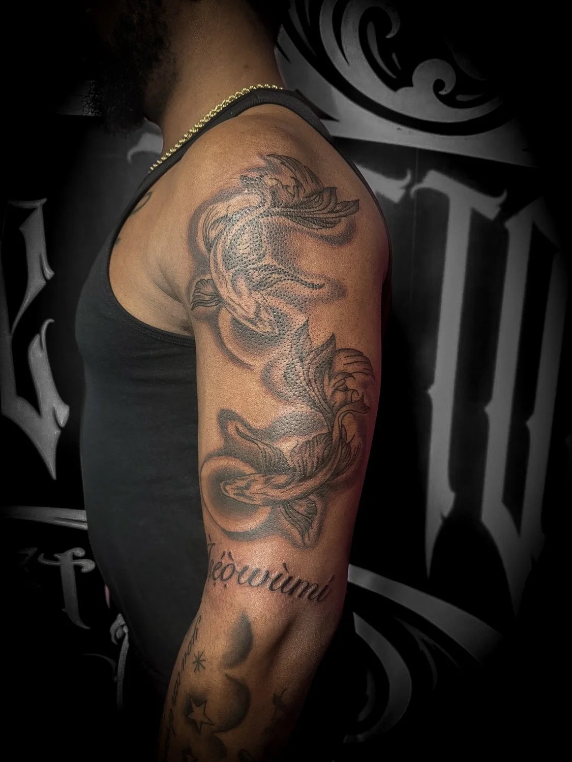 Close-up of a person's upper arm tattoo featuring a detailed fish with flowing fins, surrounded by smoke-like designs, and the word 'révolution' written below.