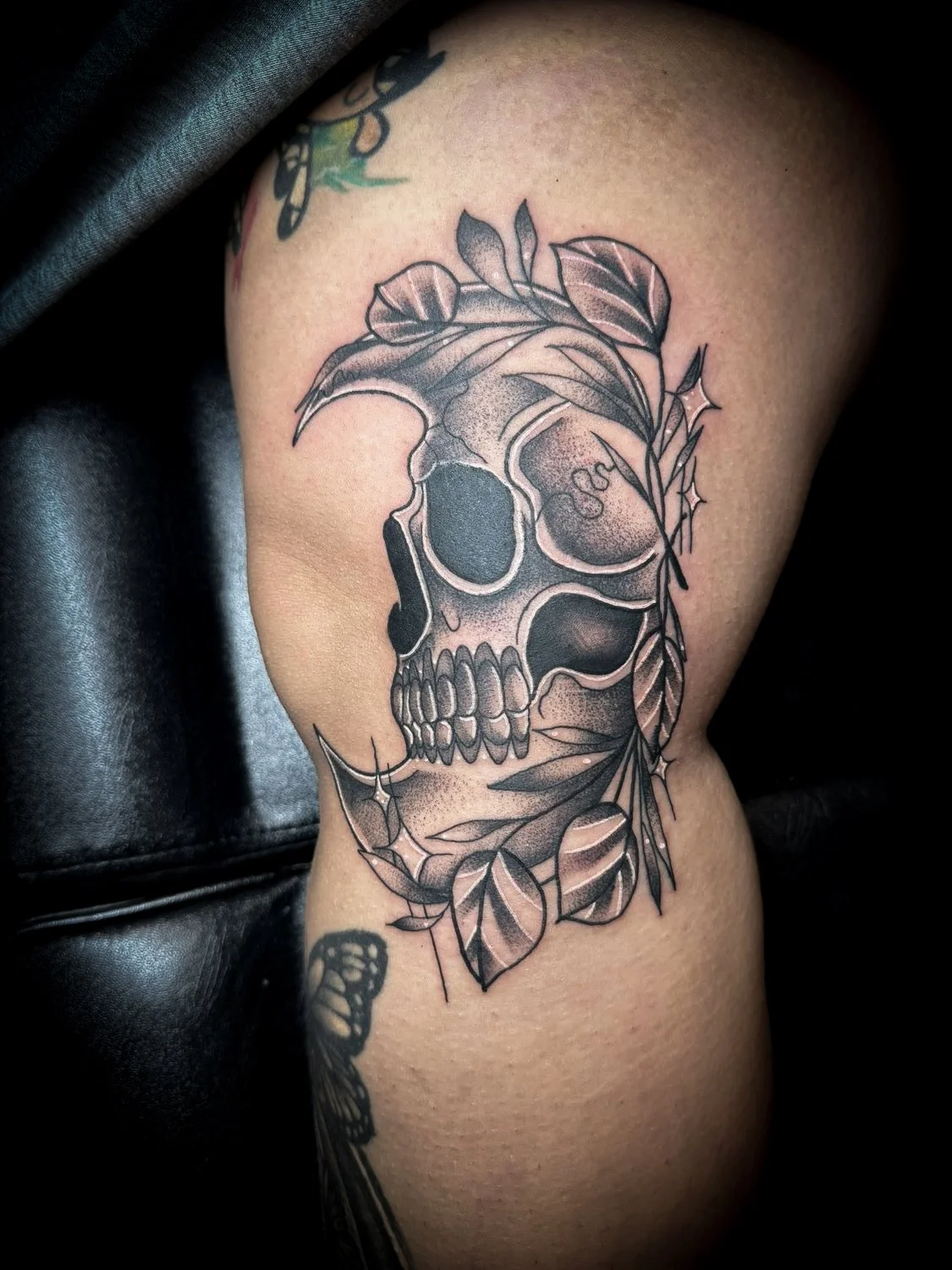 Black and gray tattoo of a skull with leaves and thorns on upper arm.