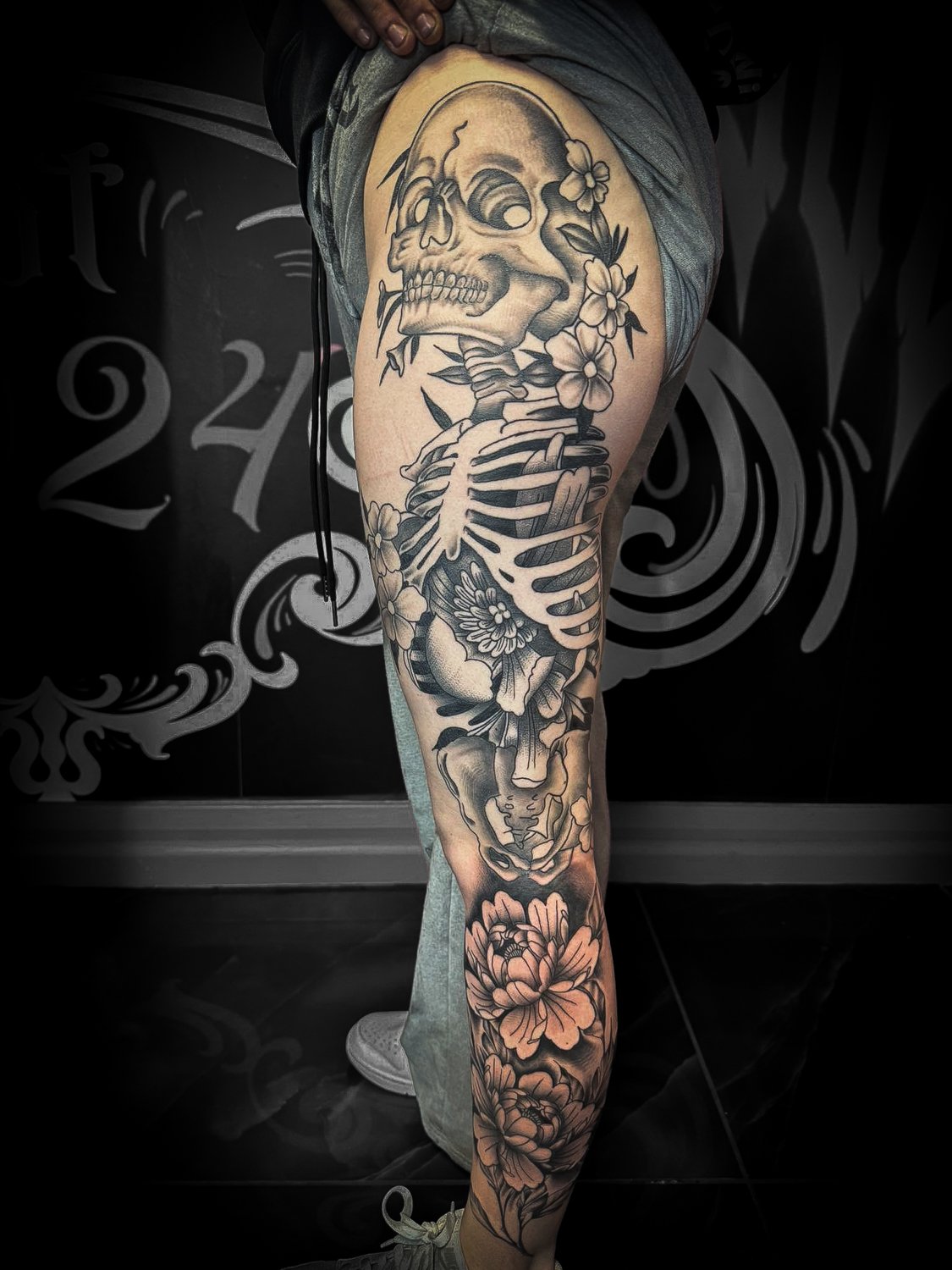 Tattoo of a human skeleton with flowers on the thigh.