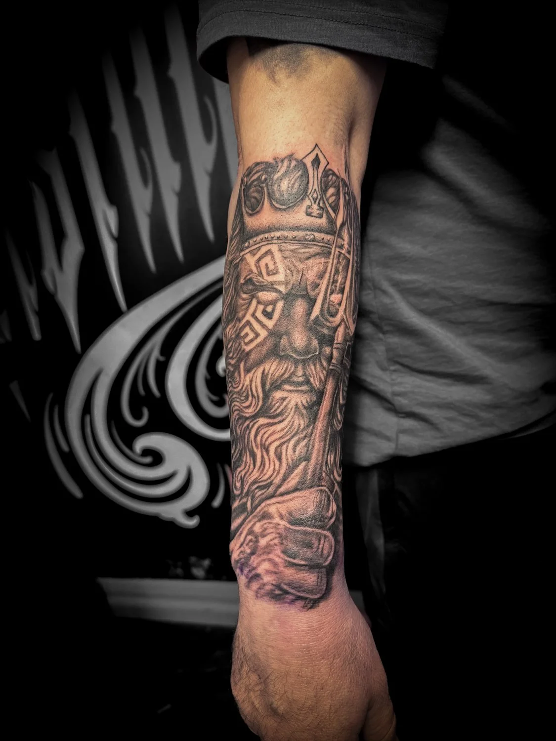 Tattoo of a bearded man wearing a helmet with goggles, holding a spear, detailed in black and gray ink on a person's forearm.