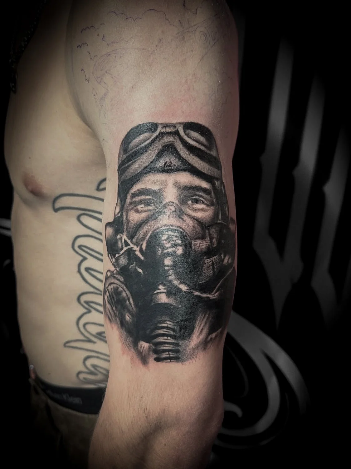 Black and gray tattoo on person's arm of a man in a gas helmet, fighter pilot.