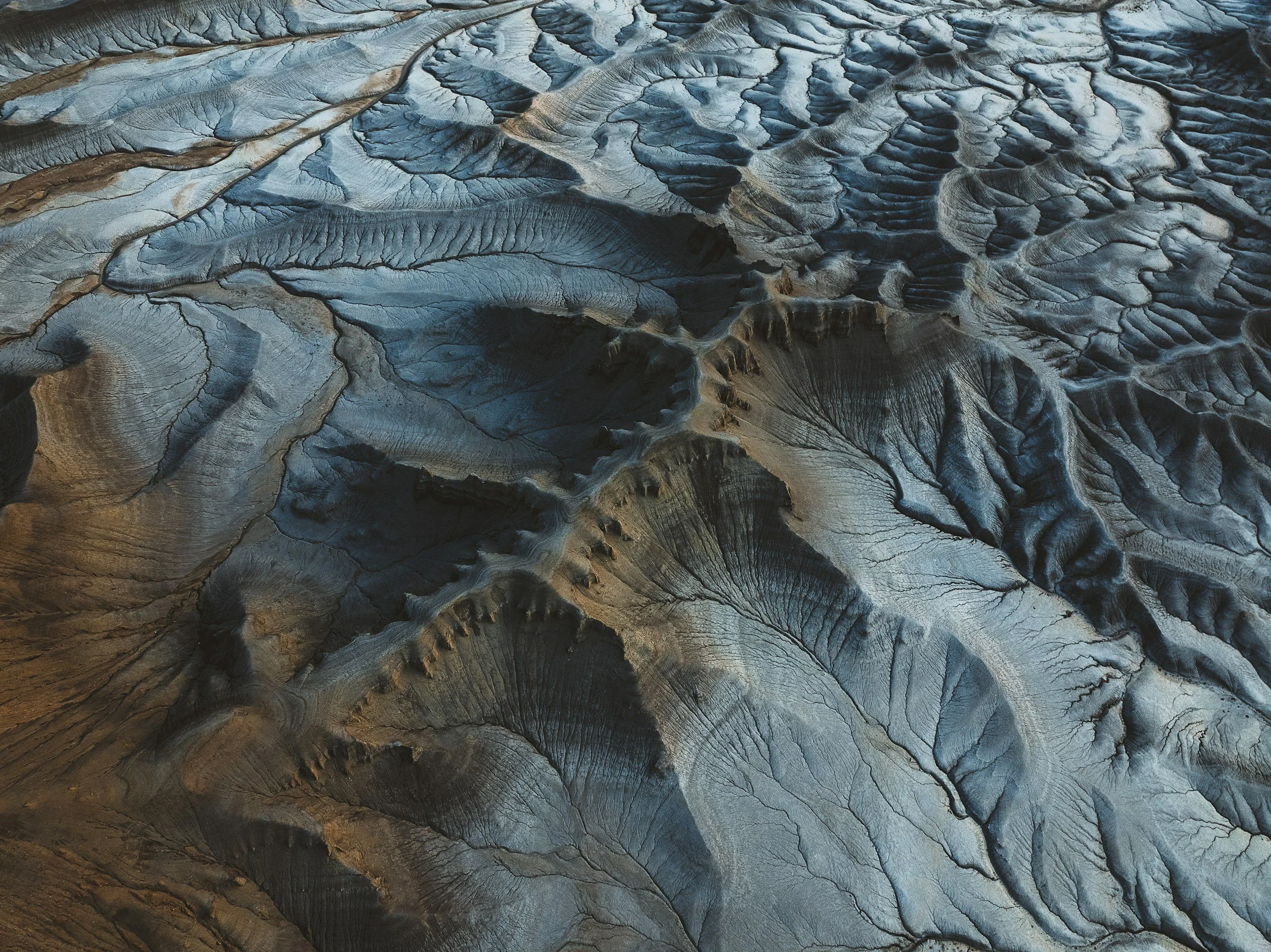 Aerial view of icy, frozen terrain with intricate patterns, cracks, and ridges in shades of gray, blue, and brown.