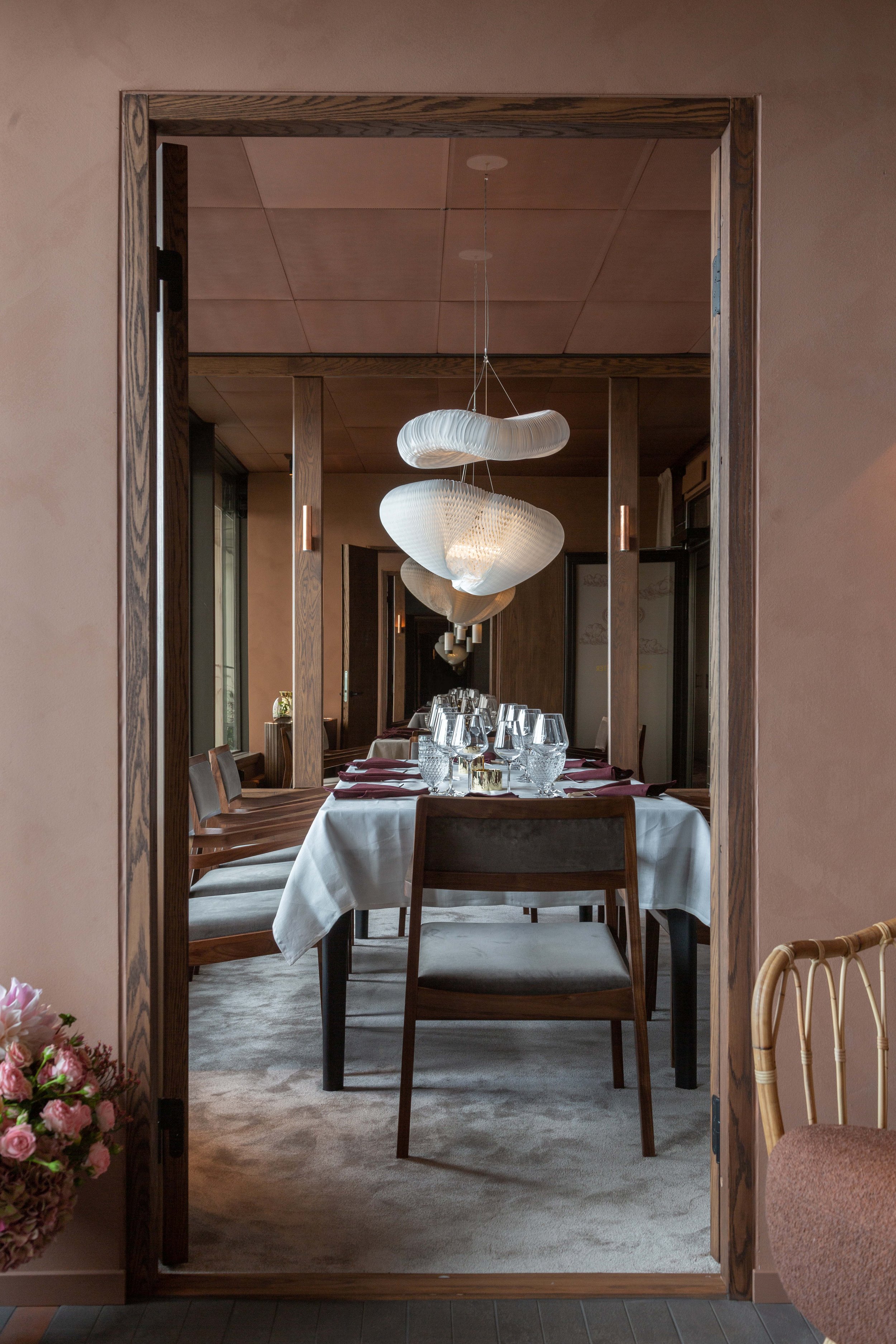 Internationell restaurang eller vardagsrum med inbjudande matbord och modern belysning, sett genom en träinramad öppning i projektet La Tour i Stockholm