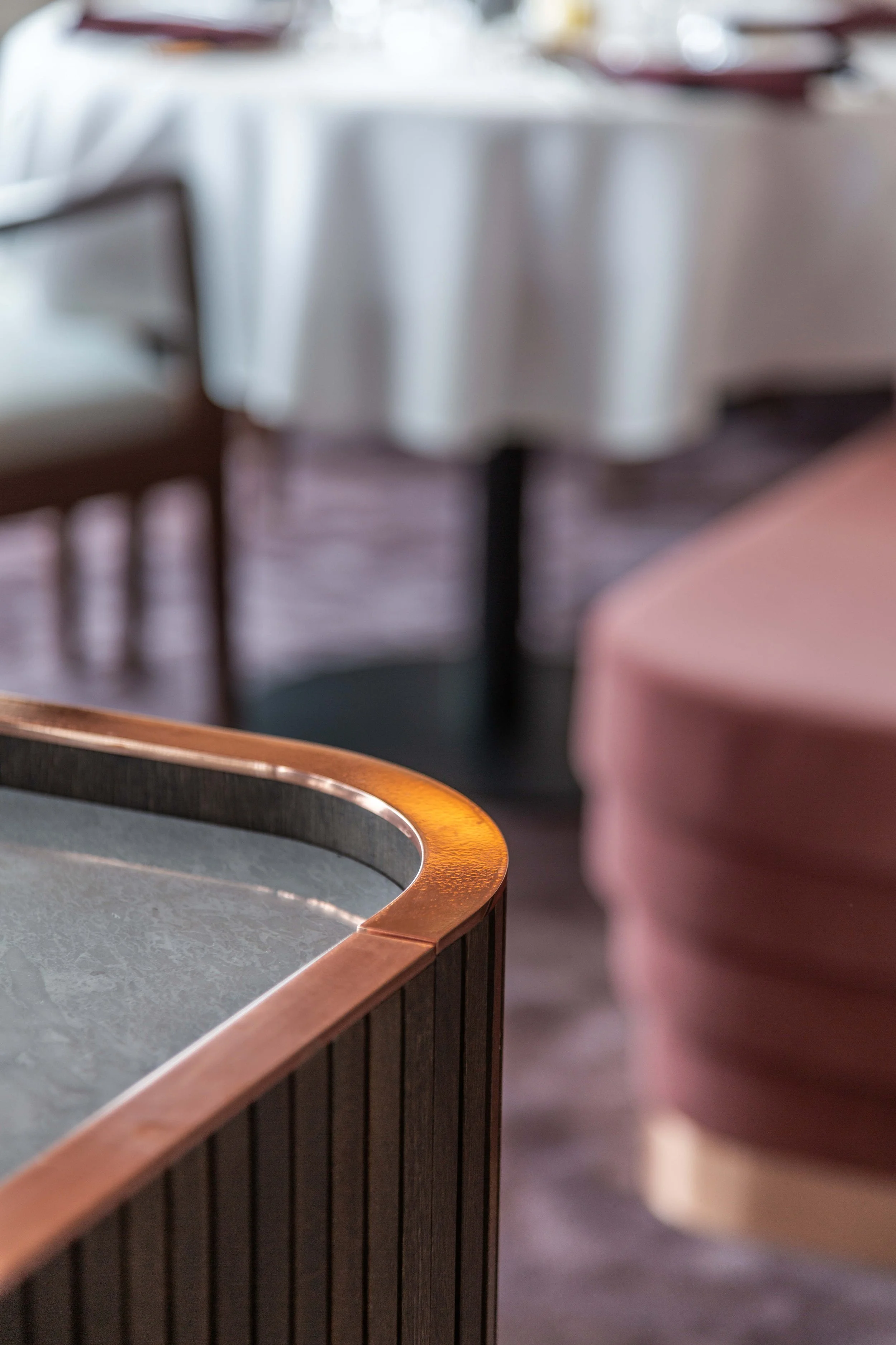 Detaljer av en bar eller ett bord i ett restaurangmiljö med vita dukar och sätter för mat, samt en del av en sittplats med ett rosa dynor.