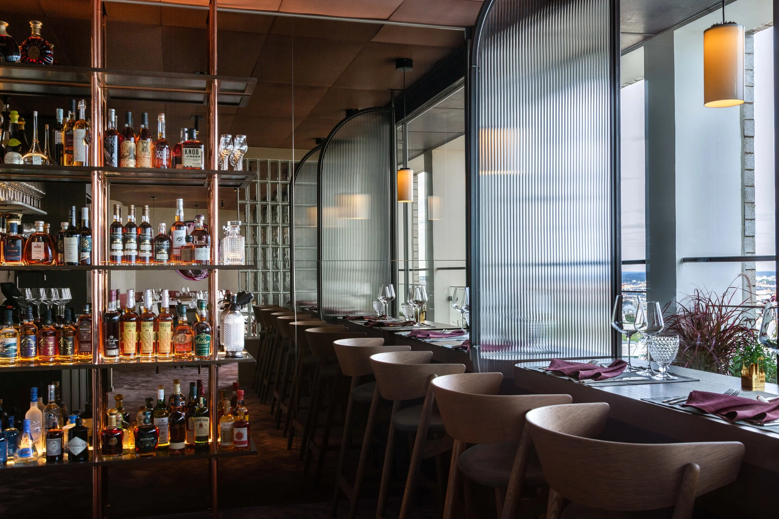 Interiör av en modern restaurang med bar i bakgrunden och fönster som släpper in naturligt ljus. Det finns bord uppdukade med glas, tallrikar och dylikt, samt stolar längs sidan i projektet La Tour i Stockholm