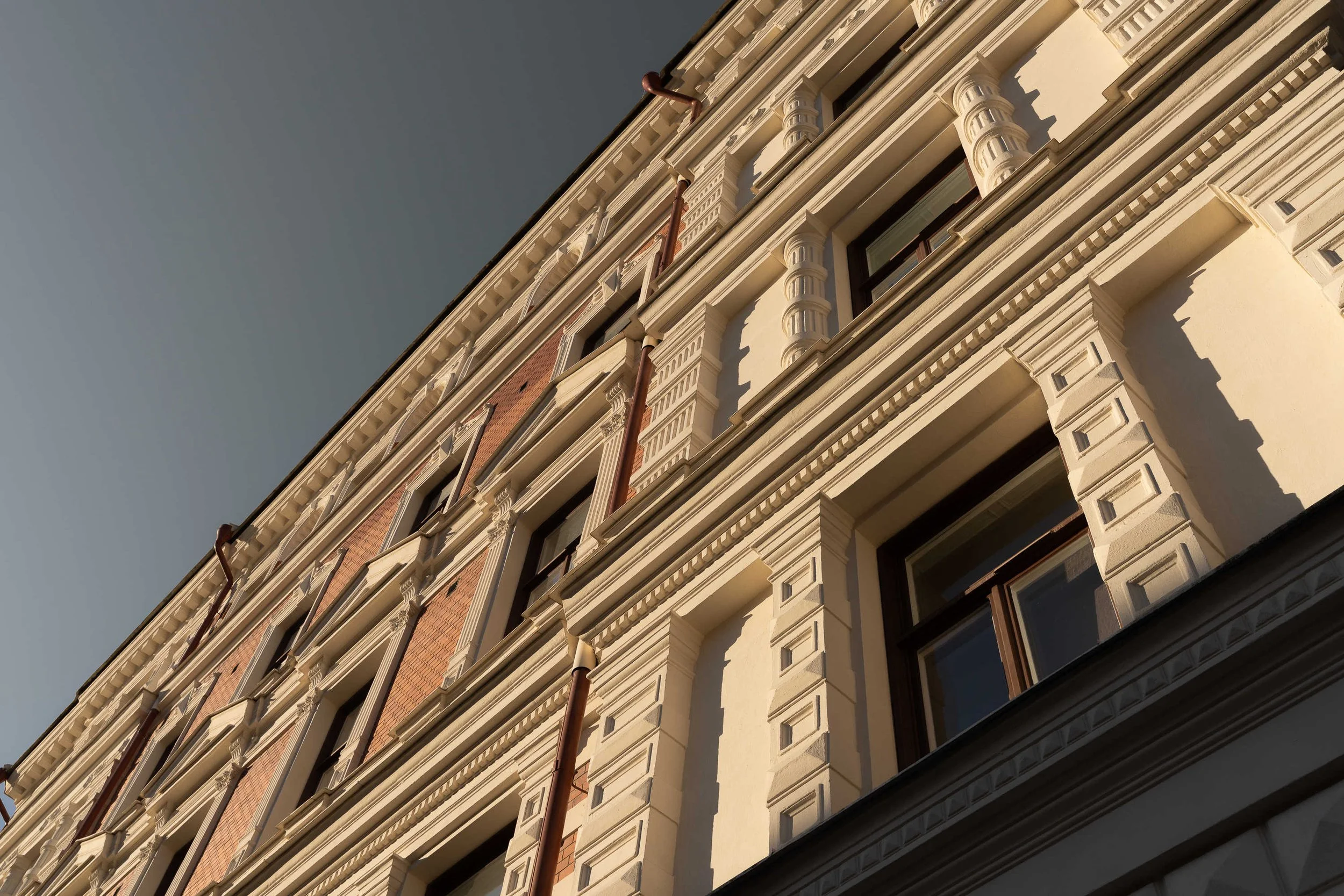 Detaljerad vy av en gammal, vacker byggnad med ornamenterade fönster och utskjutande dekorativa element på fasaden i projektet Torstenssonsgatan 12 i Stockholm
