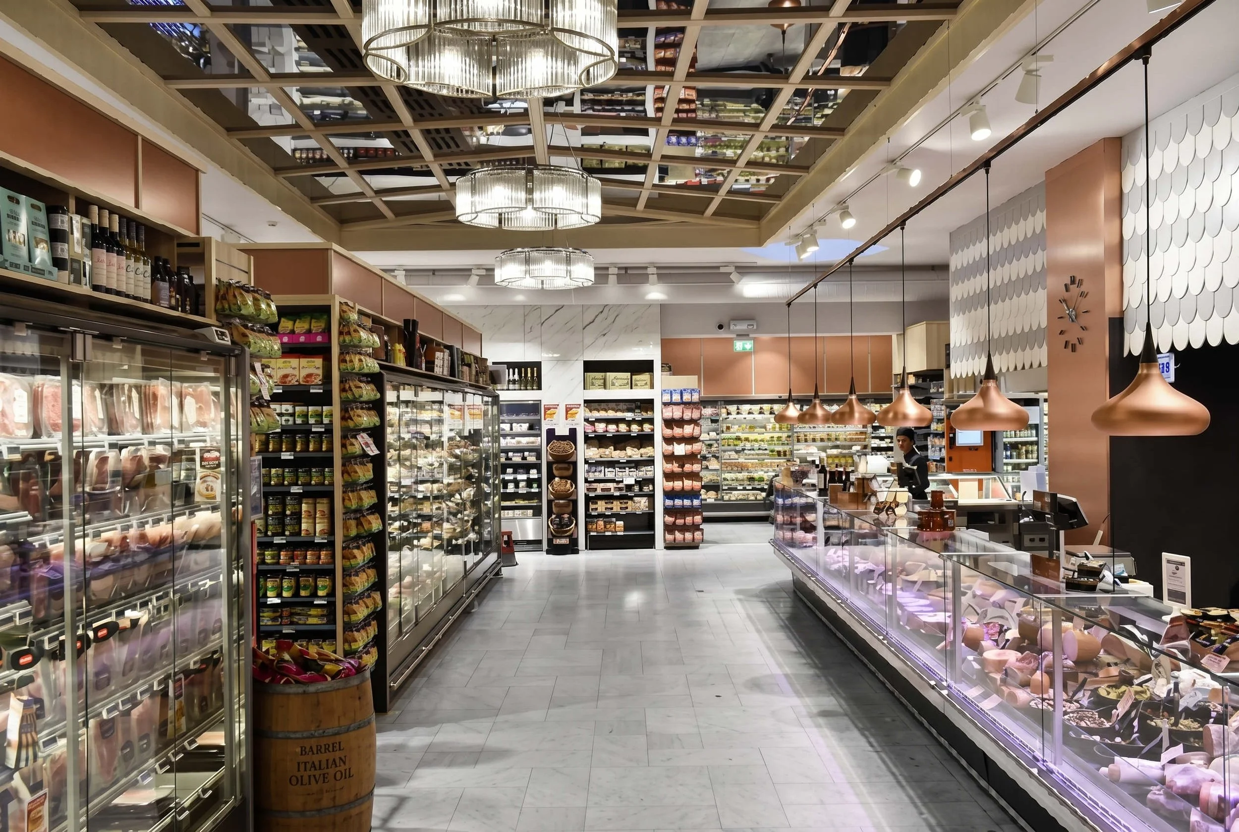 Inredning i en mataffär med kylskåp och hyllor fulla med matvaror, dekorativa taklampor och en väggklokka i projektet Ica i Stockholm