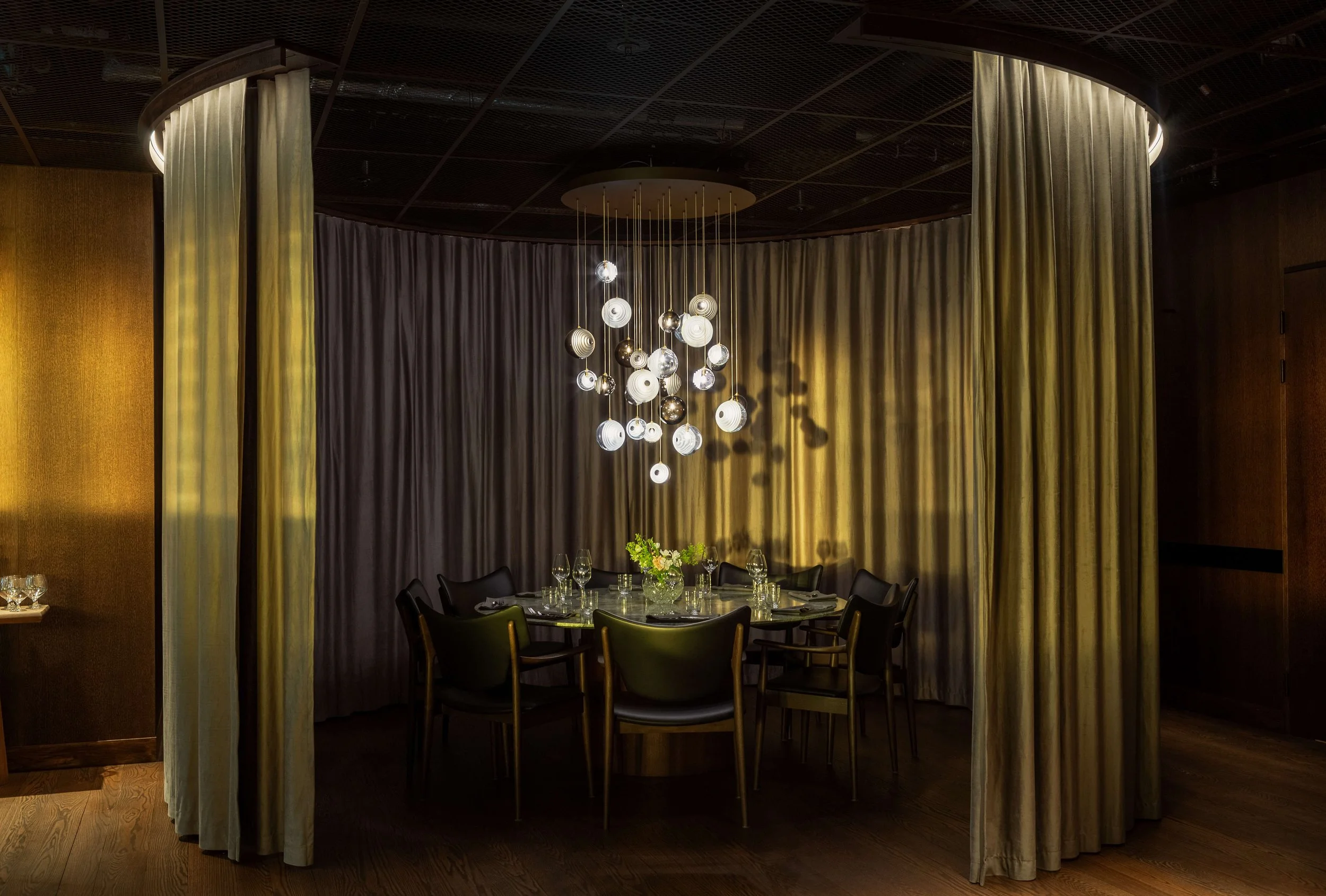 Interiör av ett elegant rum med ett runt bord, blomsterarrangemang, gardiner och en modern takkrona i projektet American Express i Stockholm Arlanda airport T5