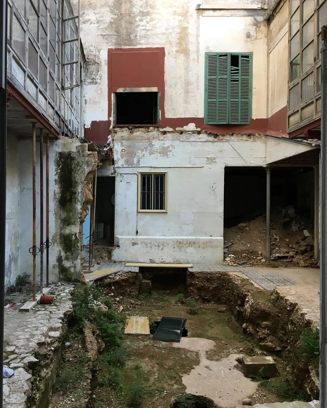 Hus under renovering eller rivning med grävning i trädgården, byggmaterial och verktyg på platsen i projektet Impremta Garden i Spain