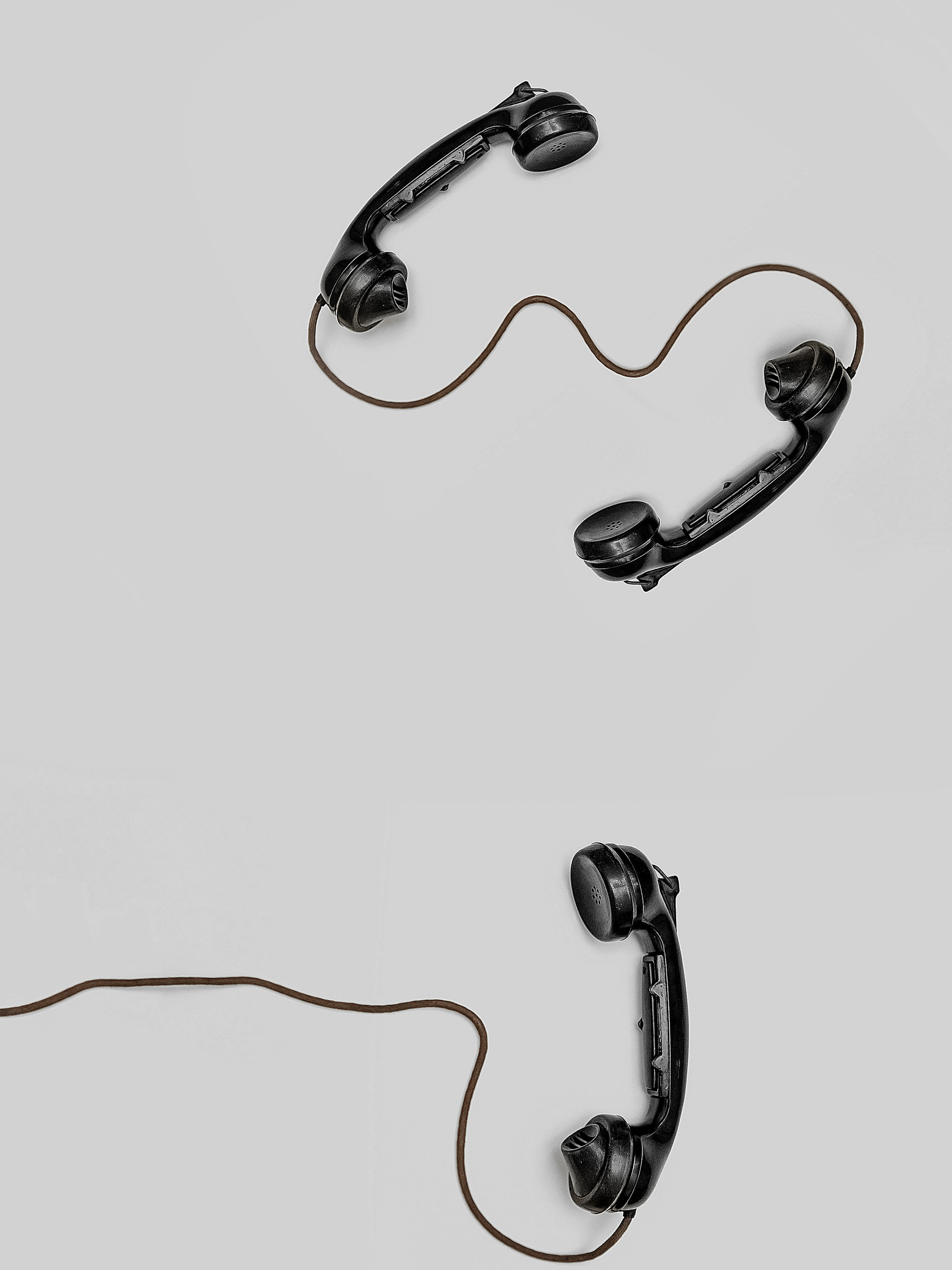 Multiple old-fashioned black telephone receivers with connecting wires, arranged on a white surface.