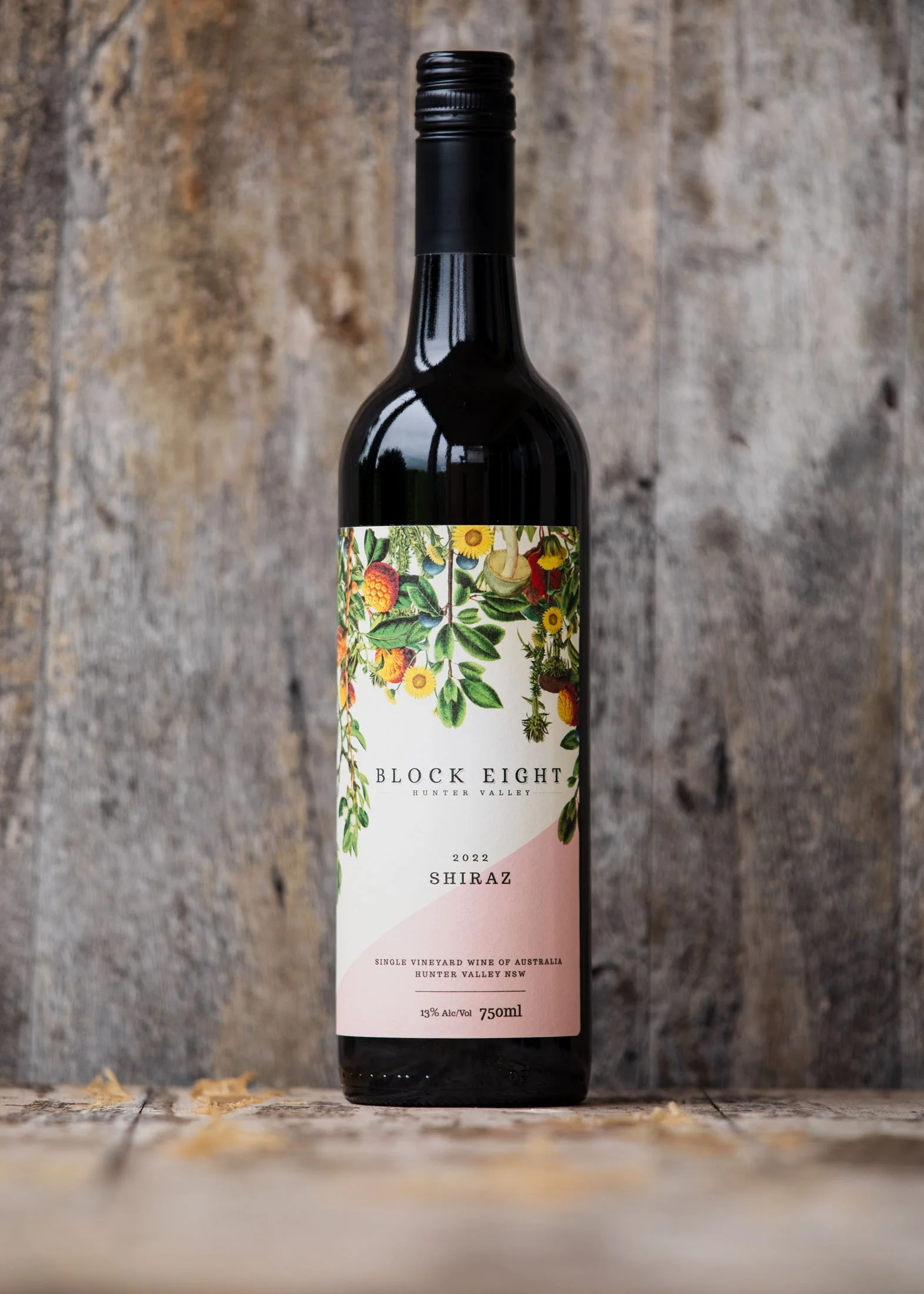 A bottle of Block Eight Hunter Valley Shiraz wine from Australia, 2022 vintage, 750ml, with a label featuring colorful illustrations of flowers and fruits, set against a rustic wooden background.