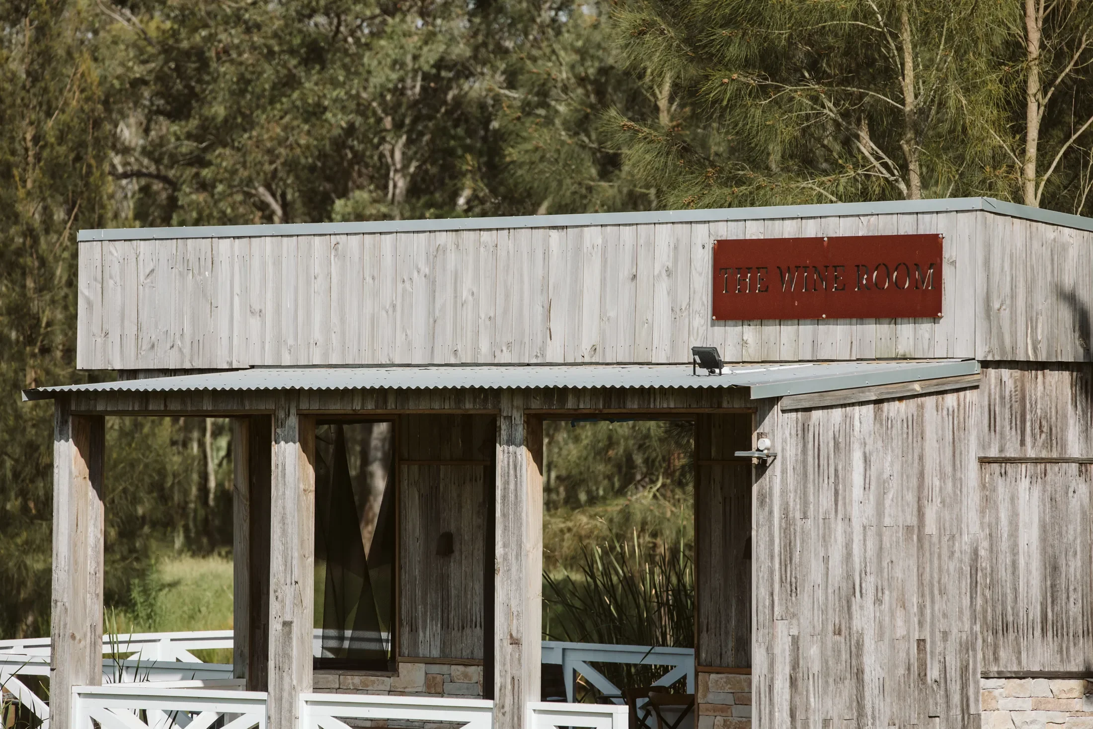 A wooden building with a sign that reads 'The Wine Room' surrounded by trees.