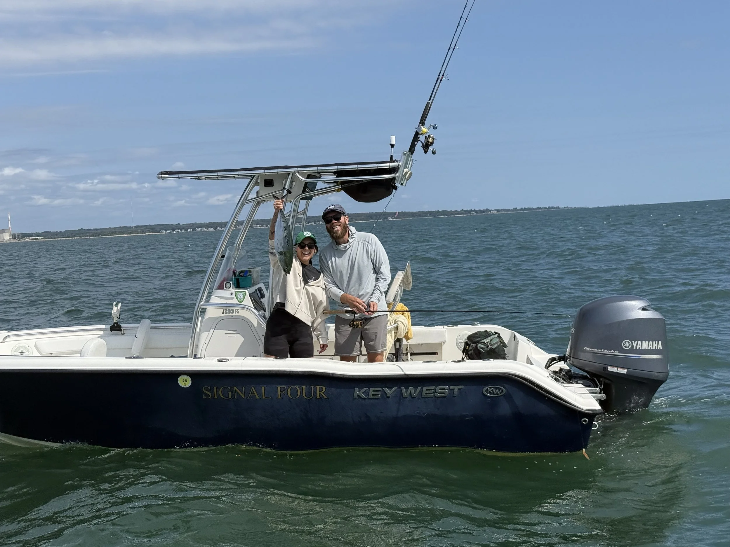 Two people on a boat holding up a fish they caught with water and sky in the background.
