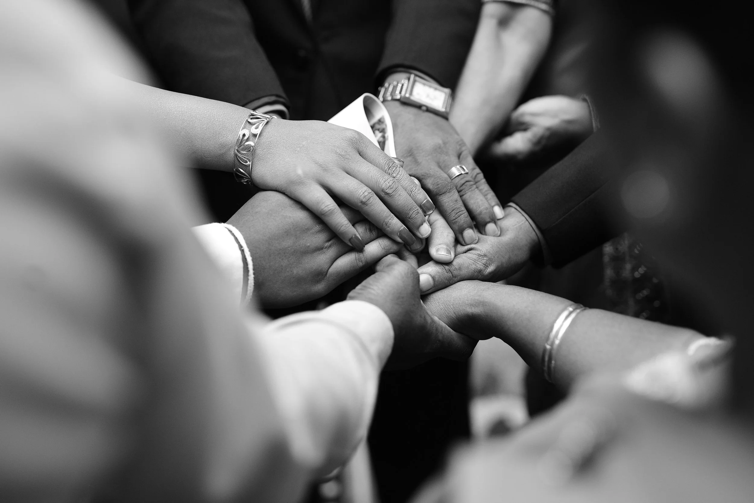 Mains jointes de plusieurs personnes en costume, symbole de cohésion d'équipe et d'unité, illustrant l'accompagnement collectif en coaching proposé par Reliences.