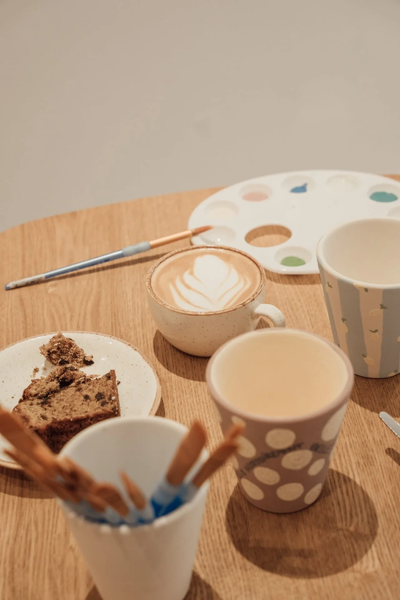 Une table avec des tasses de café, une assiette avec un gâteau, une palette de peinture, un pinceau et des gaufrettes.