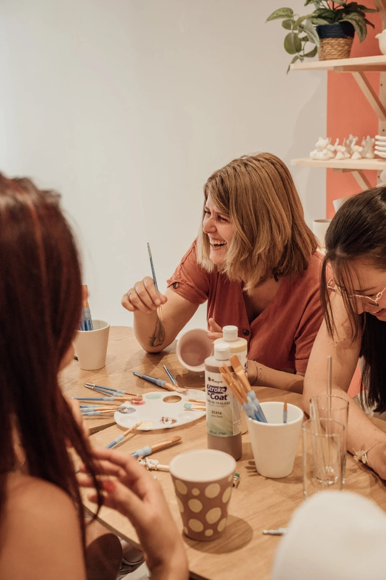 Groupe de femmes assises autour d'une table, peignant des figurines avec de la peinture et des pinceaux, semblant s'amuser et rire.