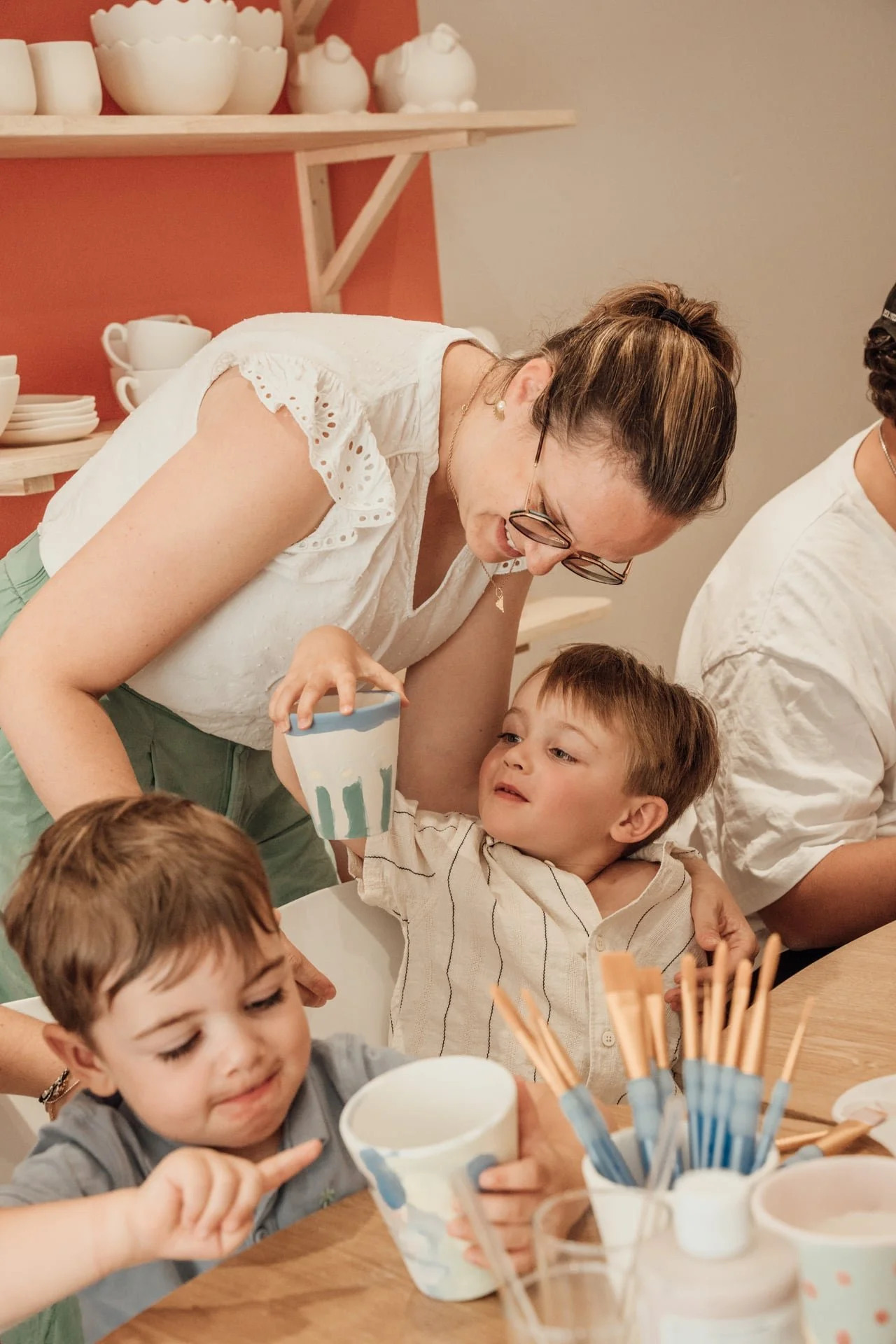 Une femme et plusieurs enfants autour d'une table, partageant un moment de convivialité et de nourriture dans un intérieur chaleureux.