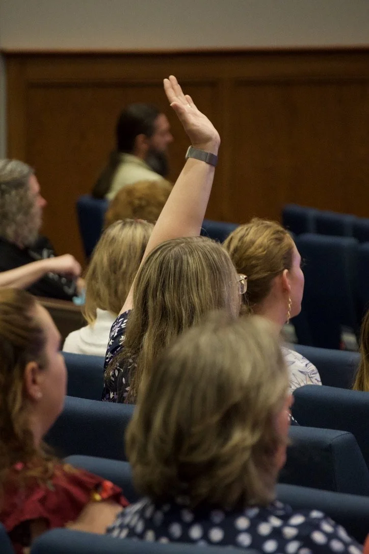 A woman in the audience raising her hand during a meeting or conference.