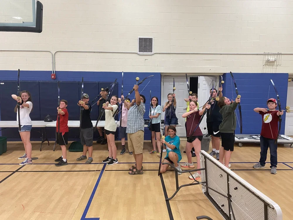 Group of children posing with bows and arrows inside a gymnasium.