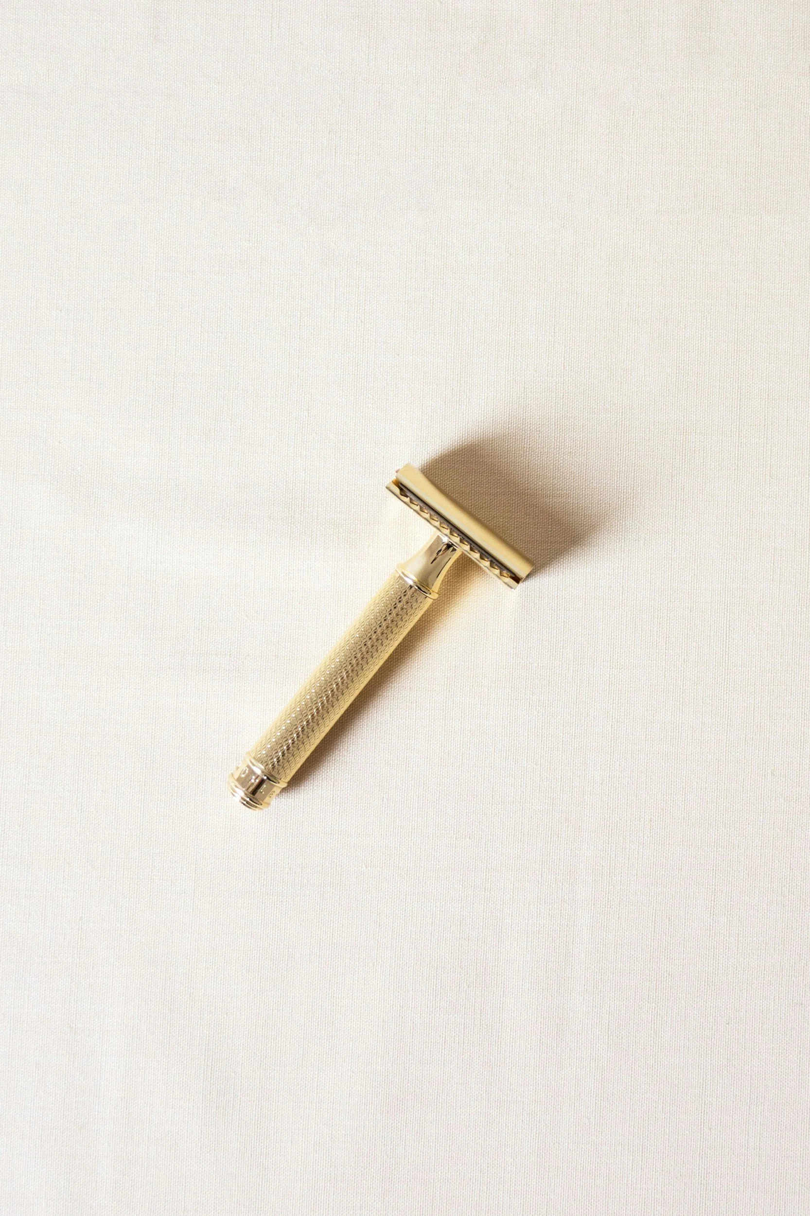 A disposable razor with a gold handle lying on a white textured surface.
