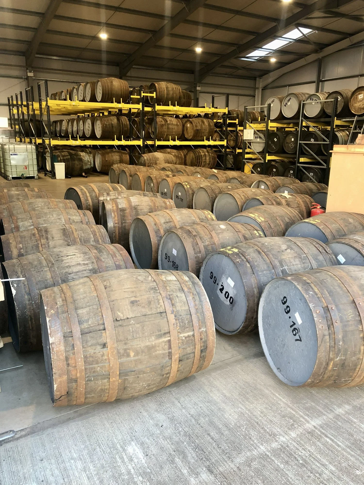 Warehouse storage with wooden casks stacked on black and yellow metal shelves and on the floor.