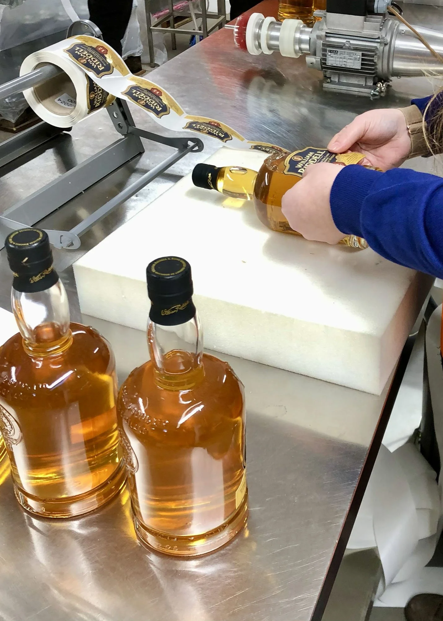 Auld Bond team member precisely labeling a whisky bottle