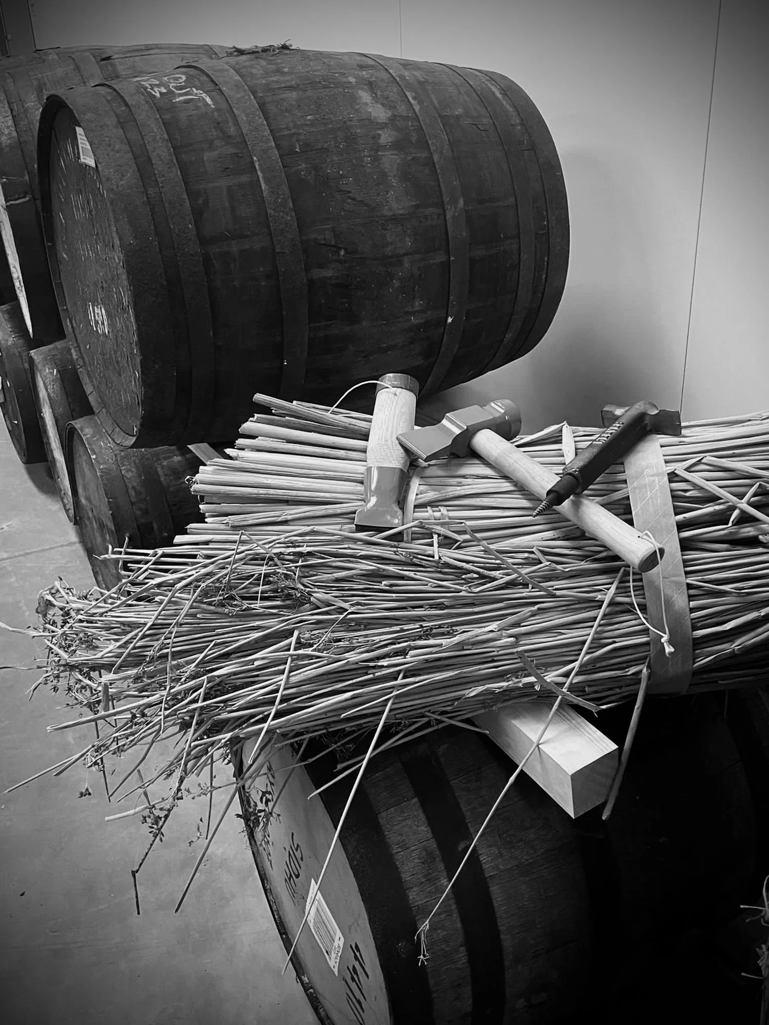 A wooden cart filled with bundles of sticks or twigs and two hammers on top, in a warehouse or storage area.