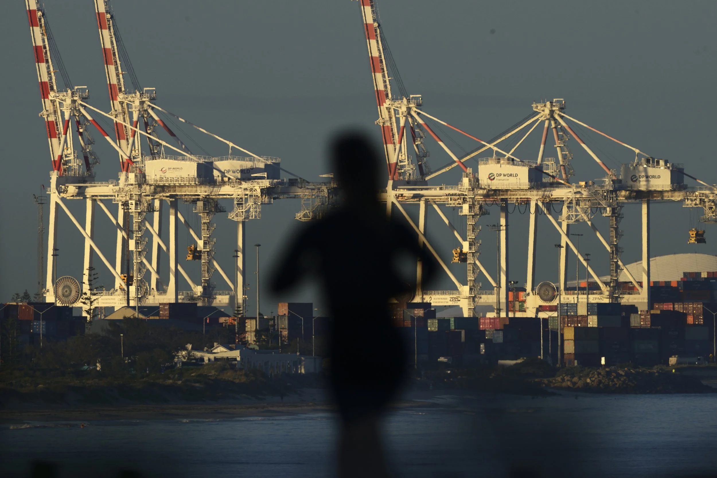 A woman runs along the coast against the background of shipping containers and cranes at the port of Fremantle, near Perth.