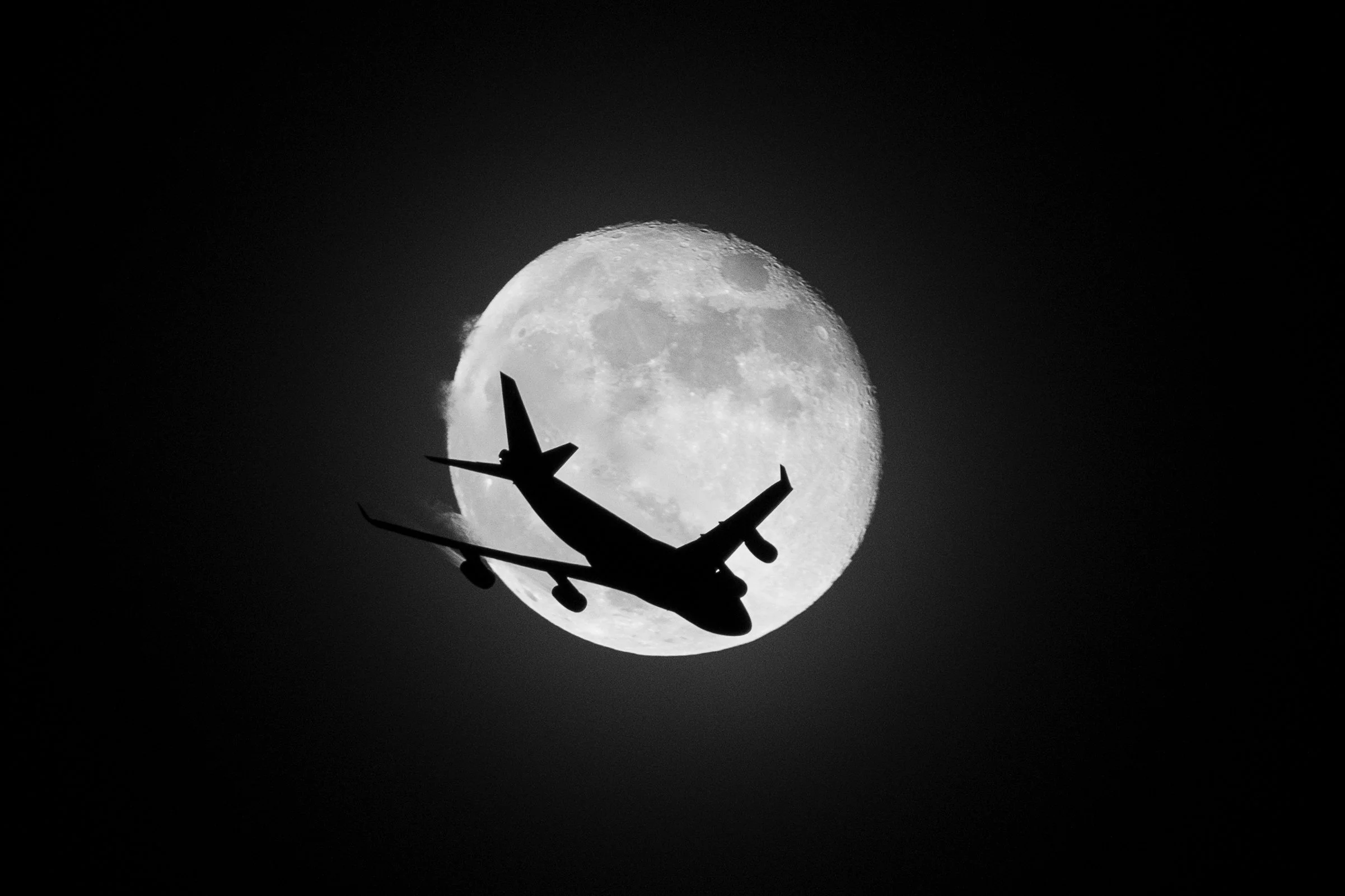 A plane flies past the full moon.