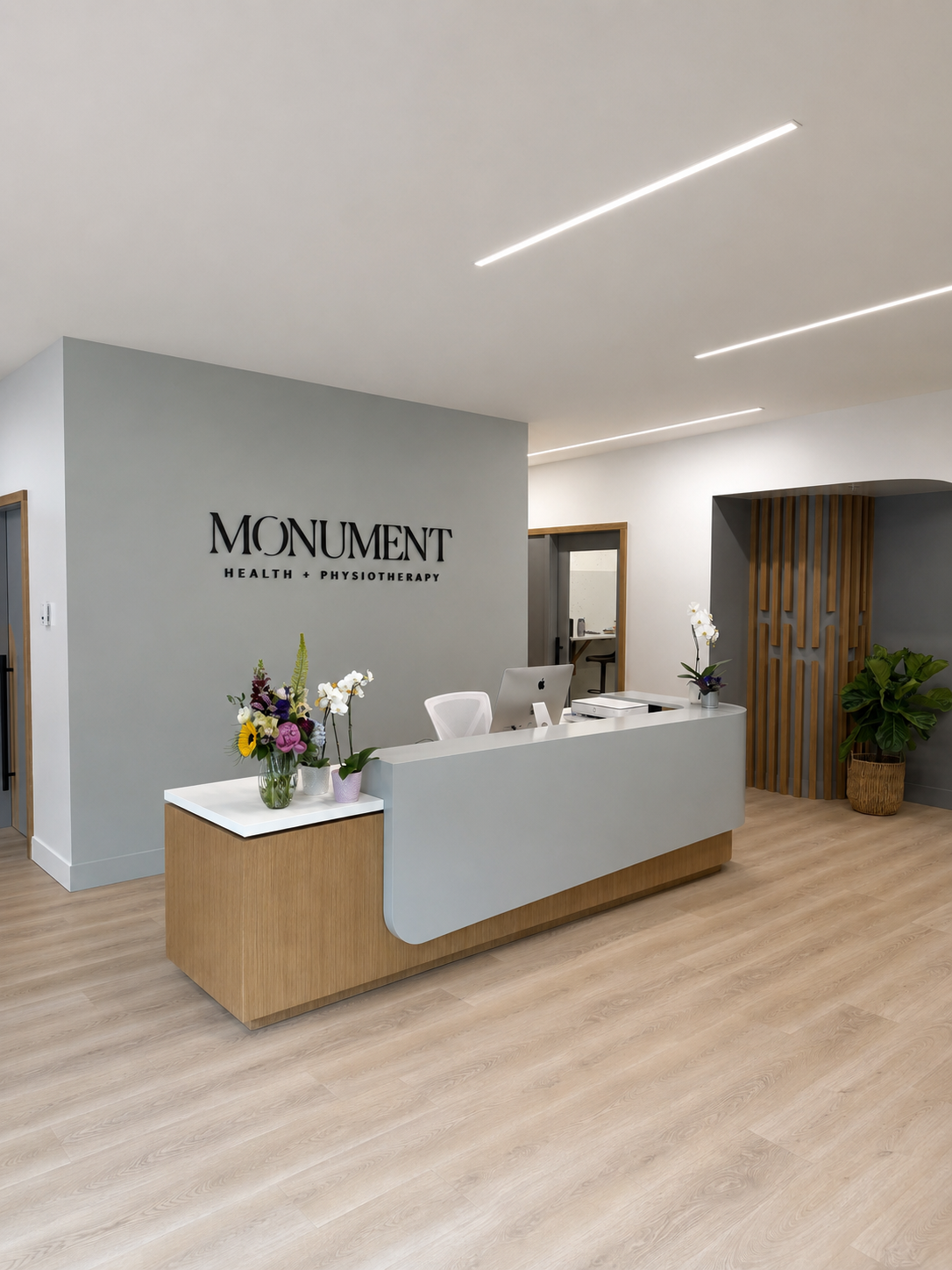 Modern reception desk at Monument Health + Physiotherapy with flowers, computer, and decorative wood paneling.