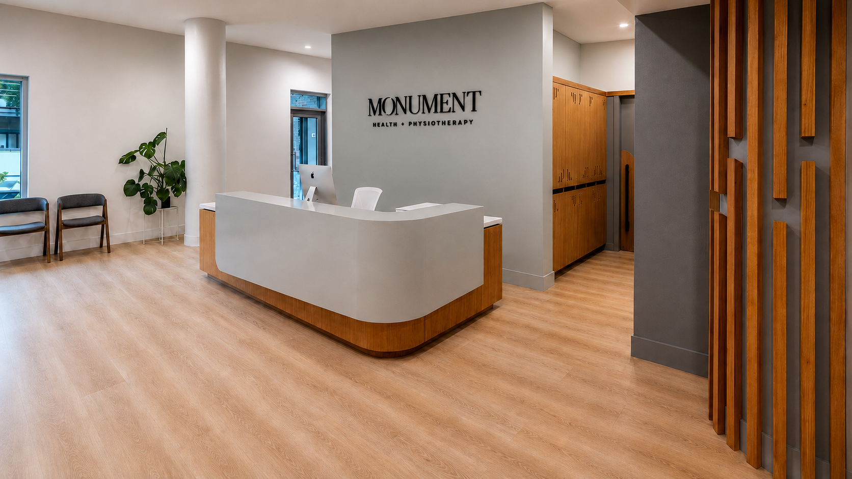 Reception area of Monument Health + Physiotherapy with a modern curved white desk, a computer, two chairs, a potted plant, and wooden lockers.