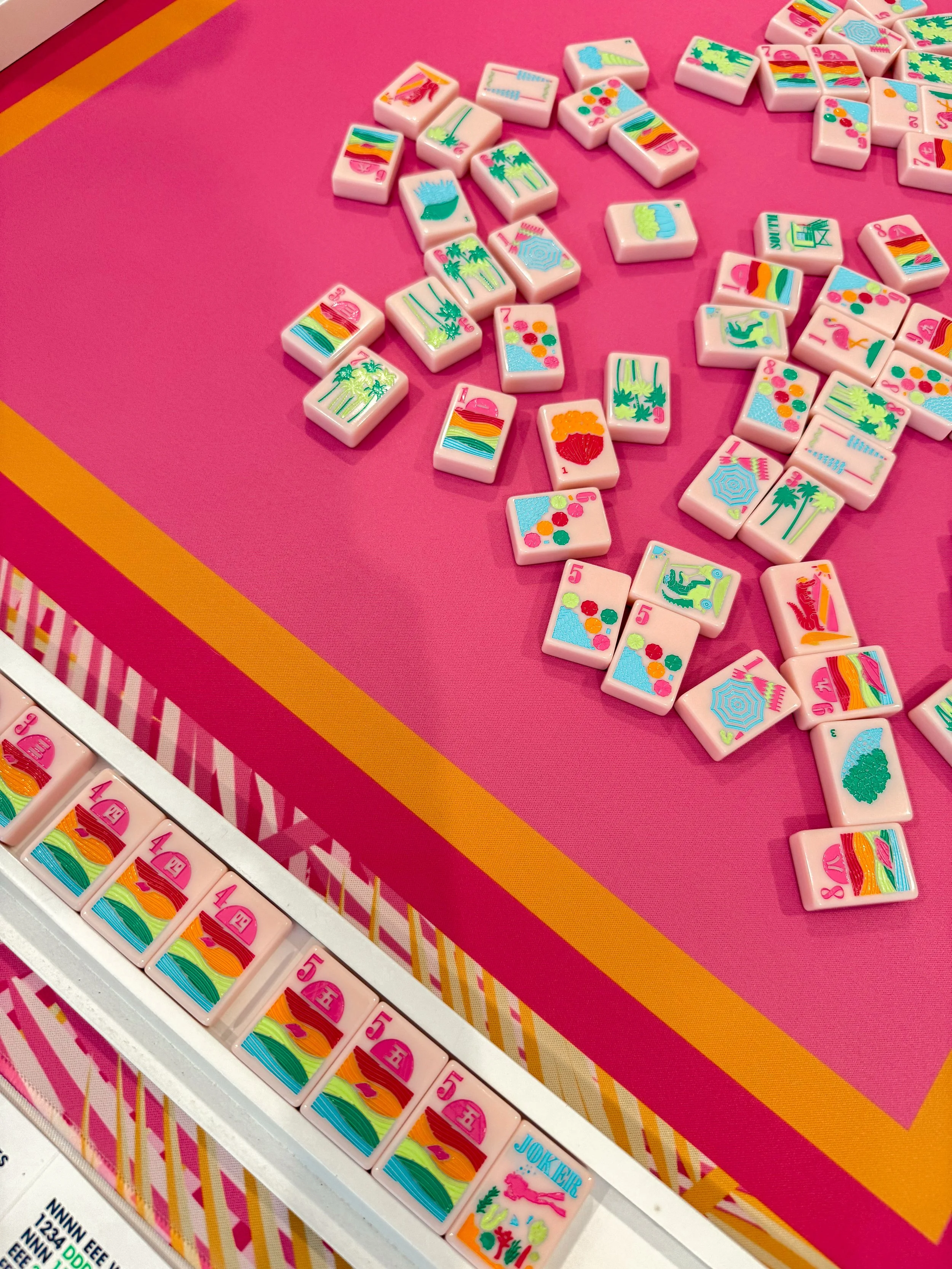 Colorful mahjong tiles with tropical and sunset designs on a pink and patterned table.