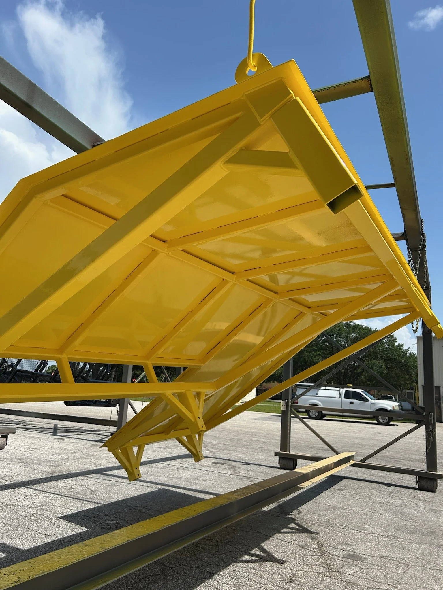 Close-up of a yellow metal structure, possibly a part of a playground or construction equipment, with a chain hanging from the top, and a blue sky with some clouds in the background.