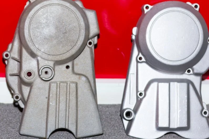 Two metallic engine timing covers placed on a surface with a red background.